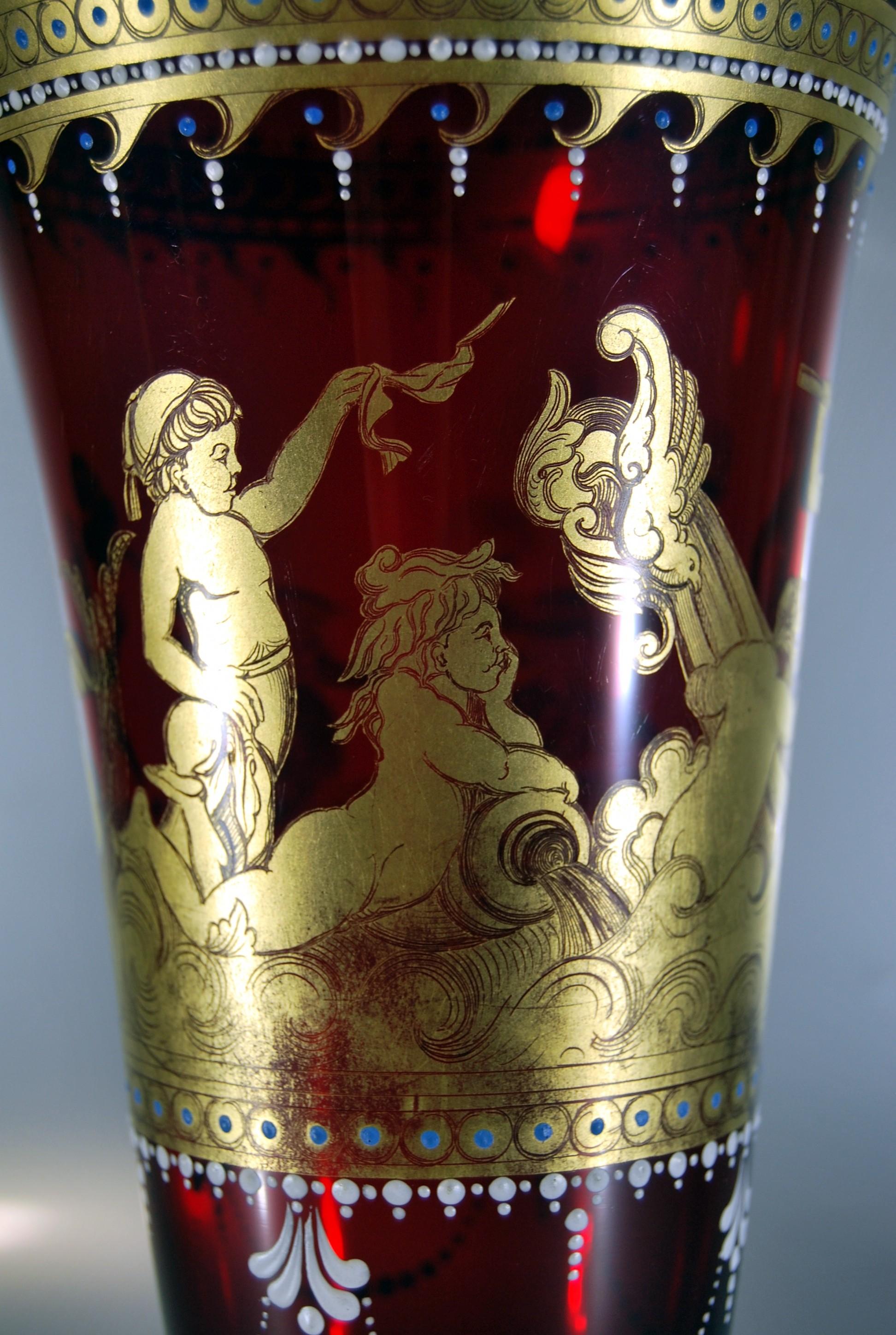 Cornet vase on pedestal in ruby glass from the beginning of the 20th century decorated at the leaf with handengraved gold and enamelled with white & blue enamel friezes. Scene of putti on the sea. no signature. Trace of pontil under the