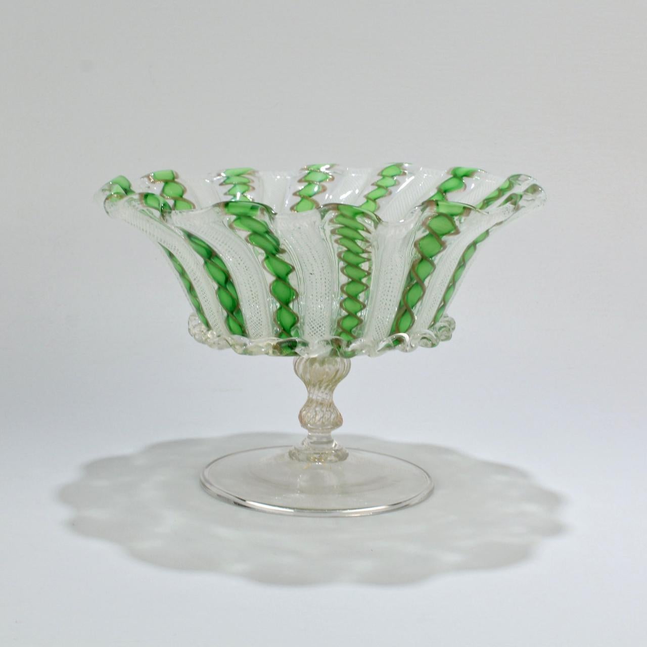 A fine Venetian glass footed bowl or compote.

With green, white, and copper color latticinio bands. The central bowl decorated with a rigaree band and supported by a blown pedestal and delicate wafer foot with inclusions.

A wonderful, delicate