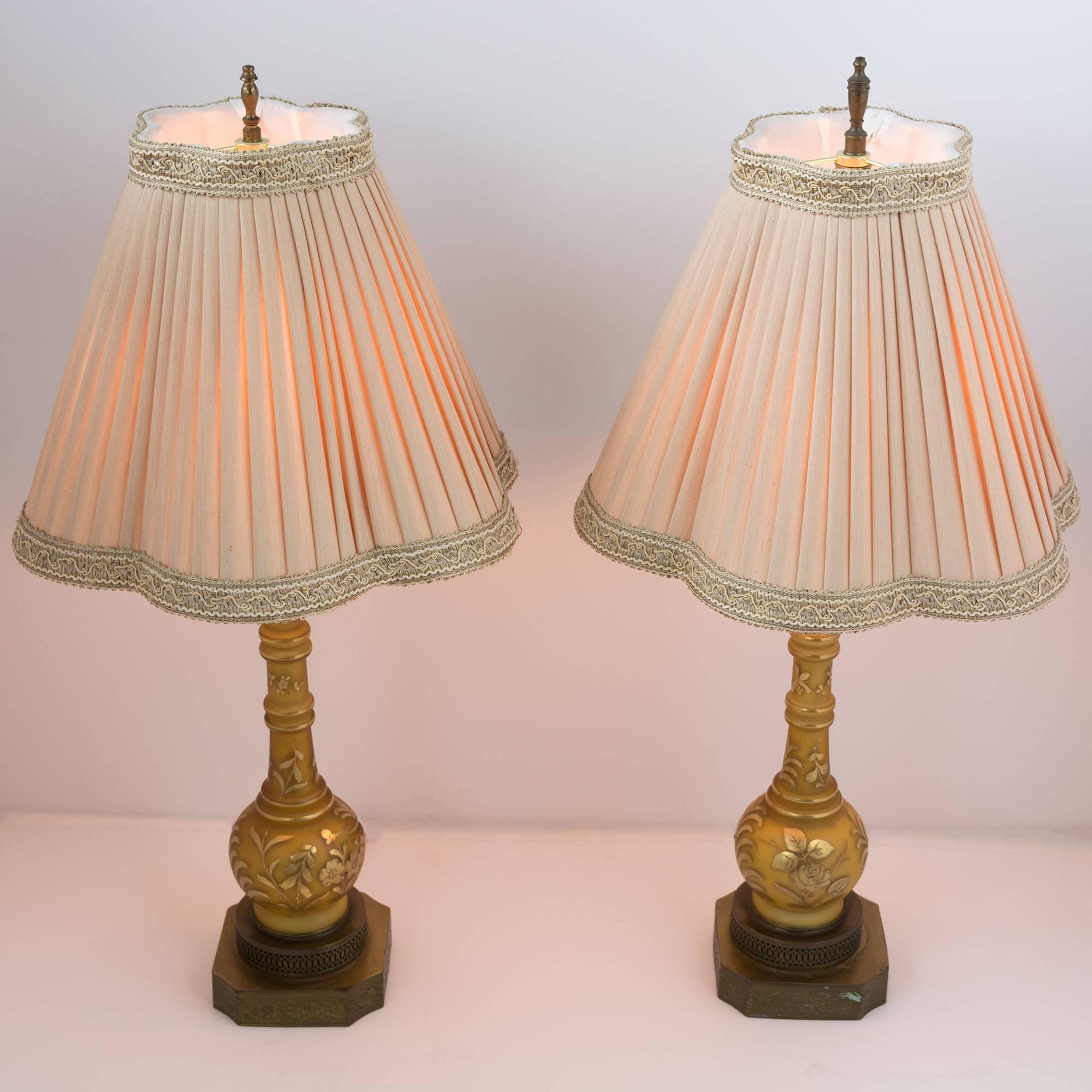 These wonderfully detailed lamps feature square bronze bases with embossed floral and cut metalwork details. The most stunning elements are the raised hand painted cameo style floral design. The shades top off the lamps in a soft pink pleated fabric