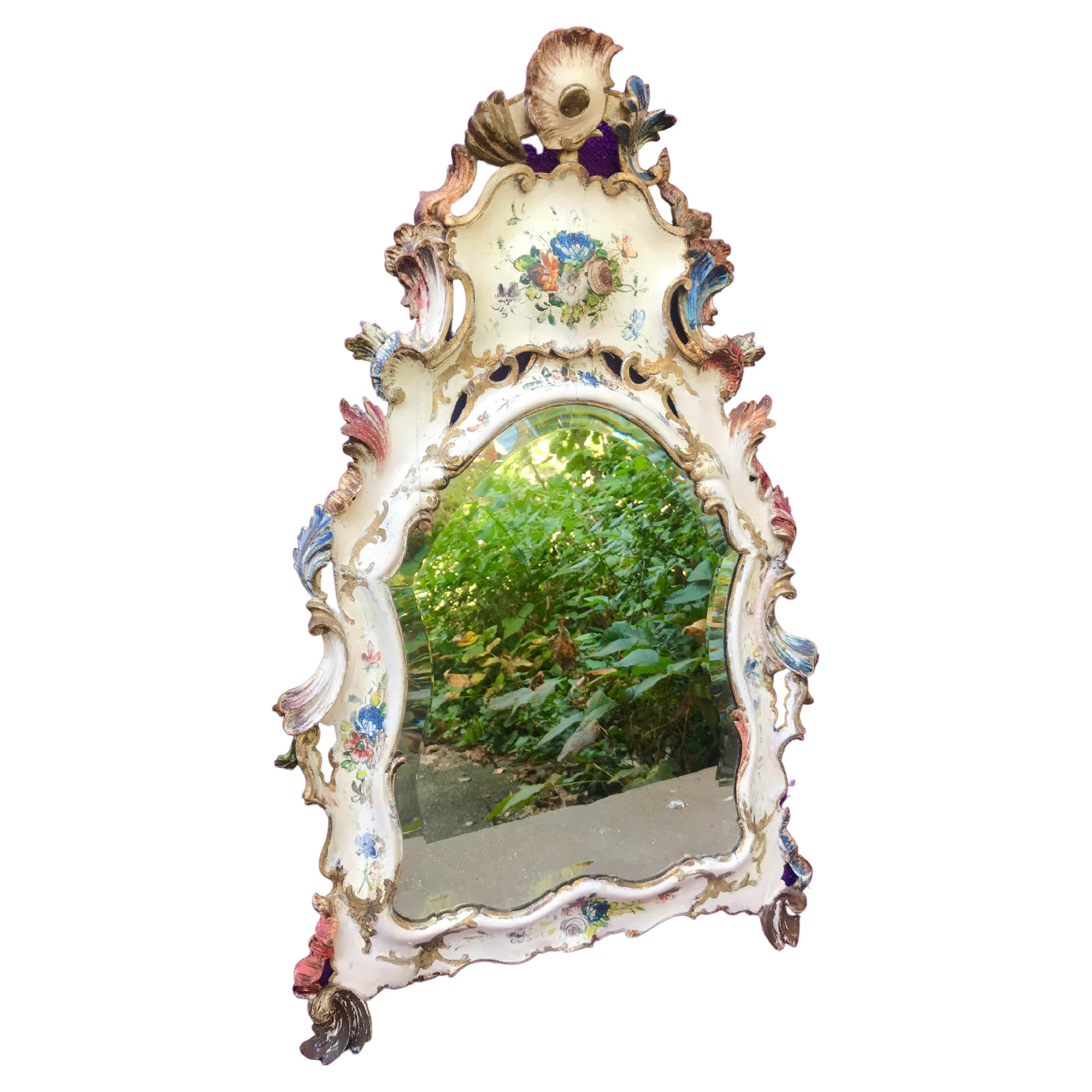 Miroir vénitien en forme de cartouche avec plaque de verre biseauté d'origine (quelques pertes dues à l'âge), bien usé de manière très charmante. Cadre en pin sculpté à la main et joint par des tendons. Cadre à décor floral peint et doré avec de