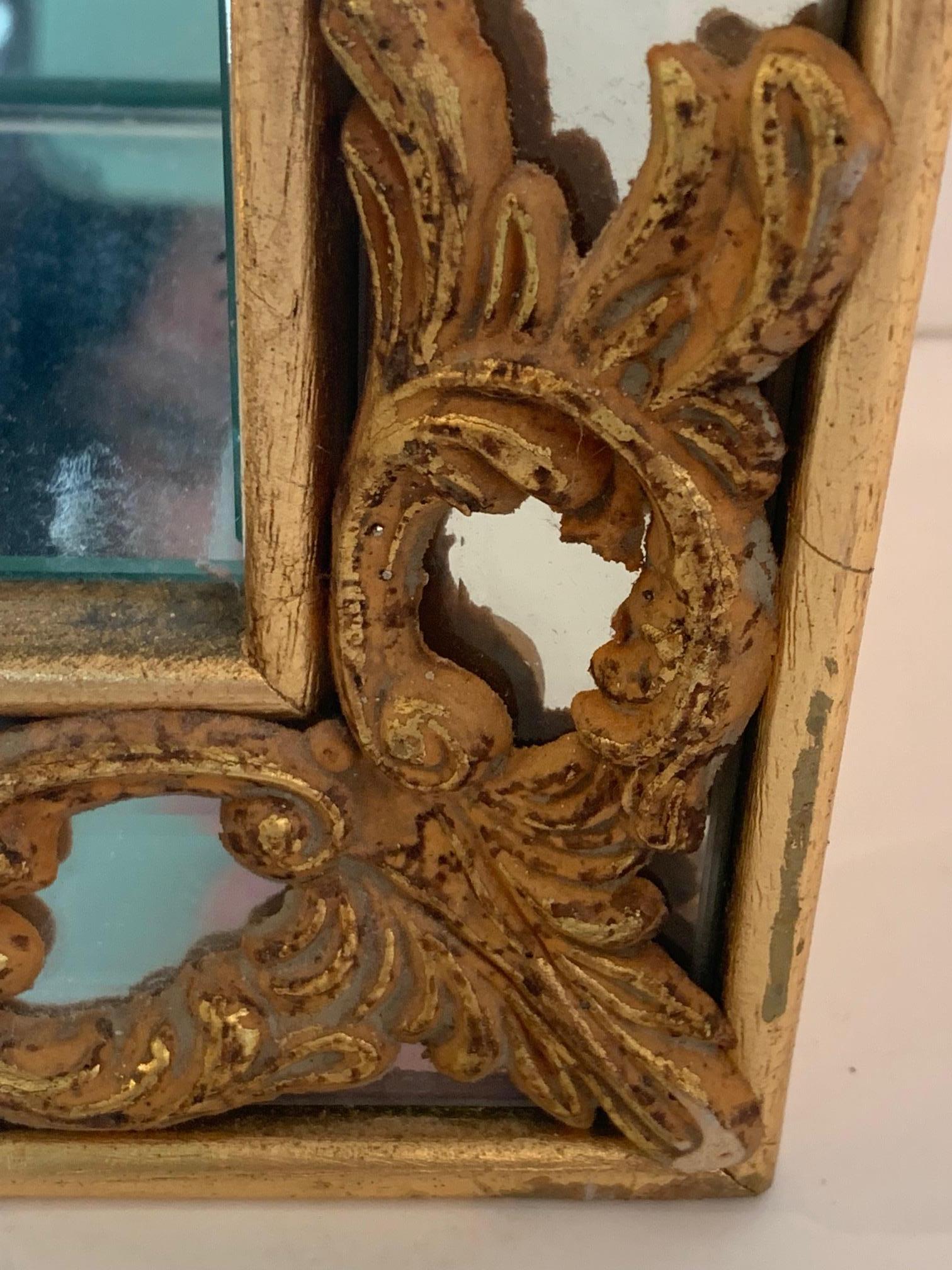 Glitzernde venezianische Hängevitrine aus vergoldetem Holz und Spiegeln, die eine rechteckige Schattenboxform mit schönen geschnitzten Goldverzierungen in jeder Ecke hat. Aus dem Innenraum ragen zwei Glasböden hervor, auf denen besondere Gegenstände