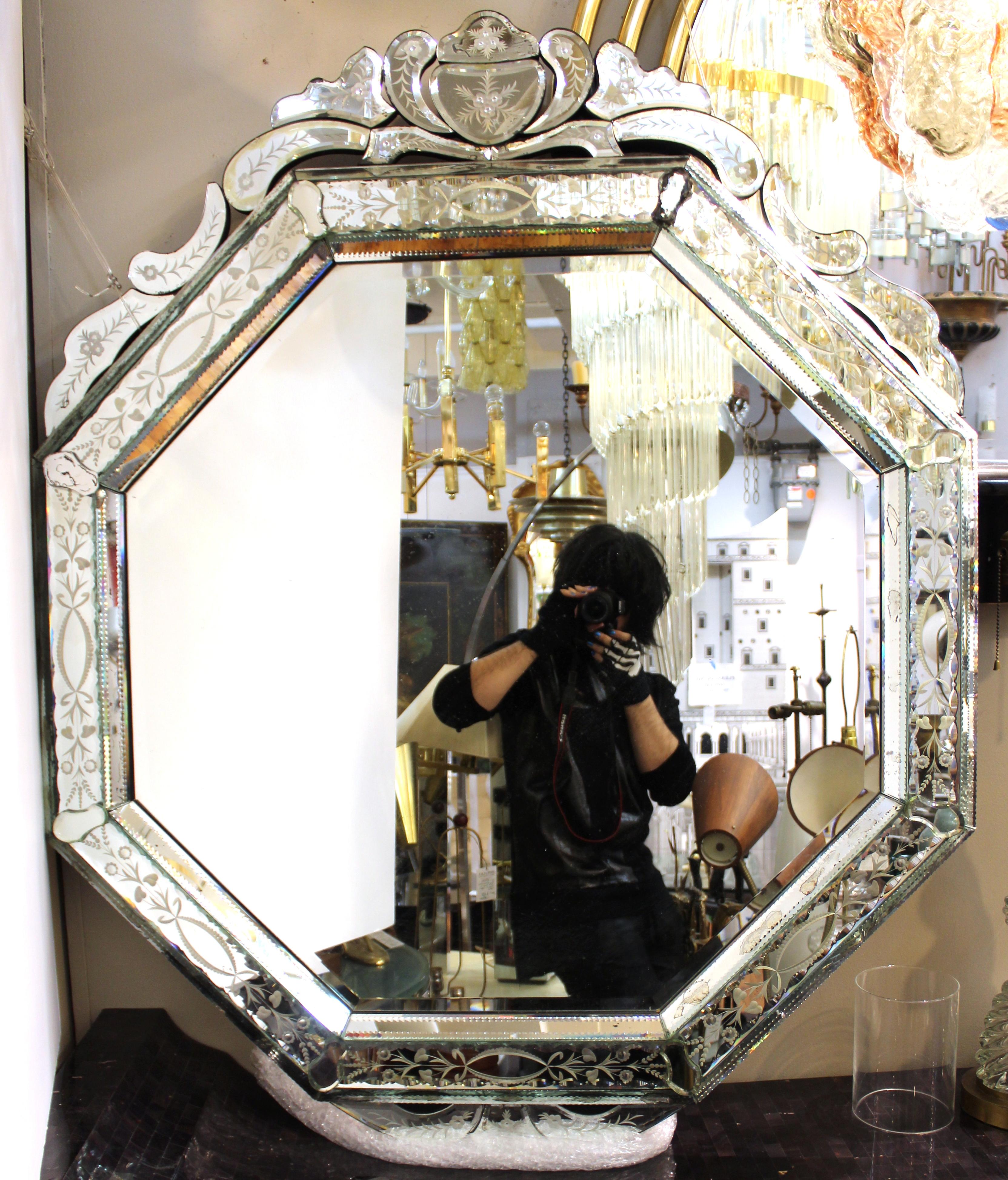 Italian Hollywood Regency period wall mirror in octagonal shape, with a highly decorative border with etched floral designs and a crest on the top. The piece was made in Venice during the early 20th century and is in great vintage condition with