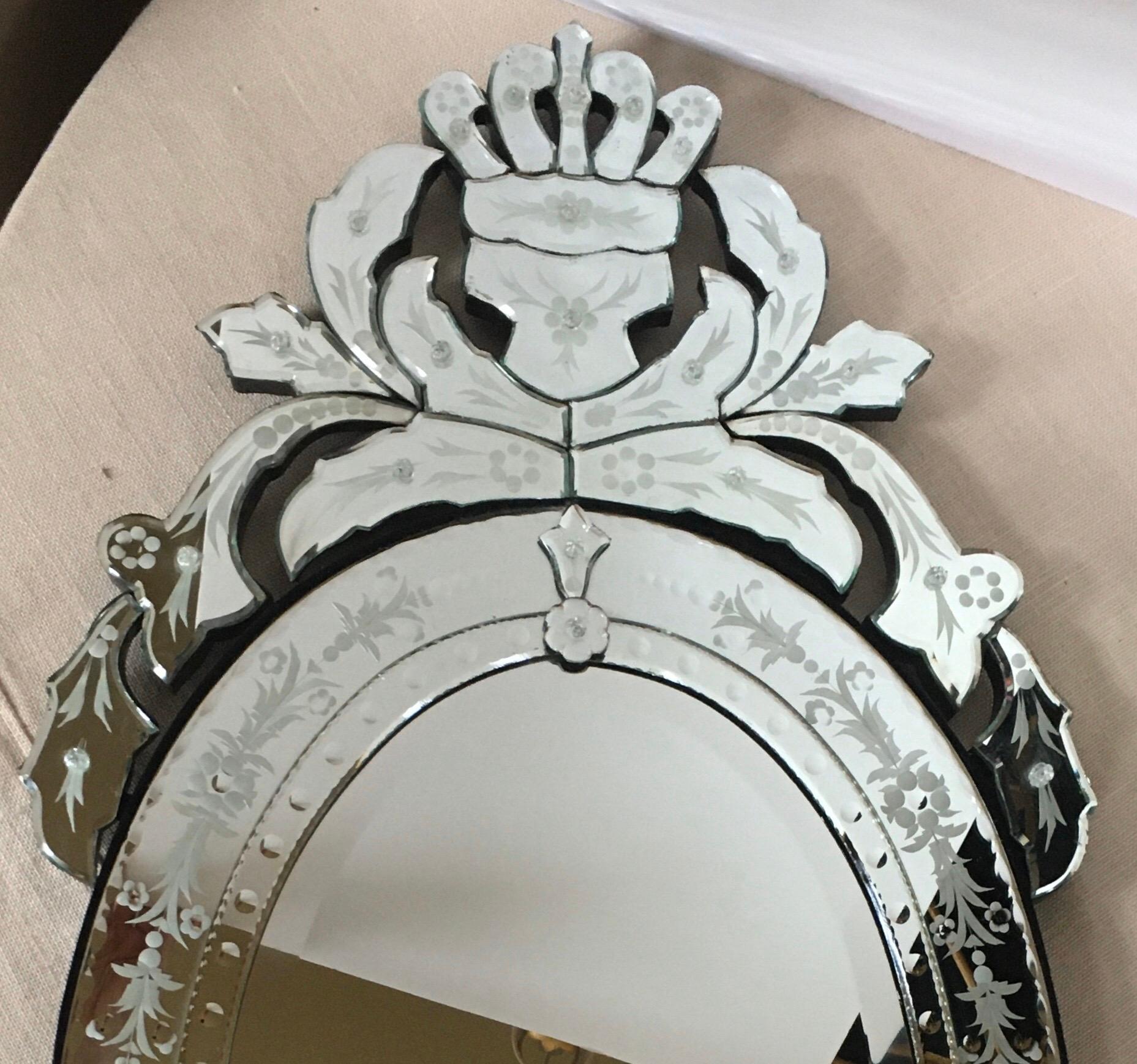 Large oval Venetian Hollywood Regency style decorative wall mirror with beveled and scalloped detailing. This elegant mirror features superbly etched floral motifs and beveled edges with a contoured crown-like crest and a large leaf-shaped pediment