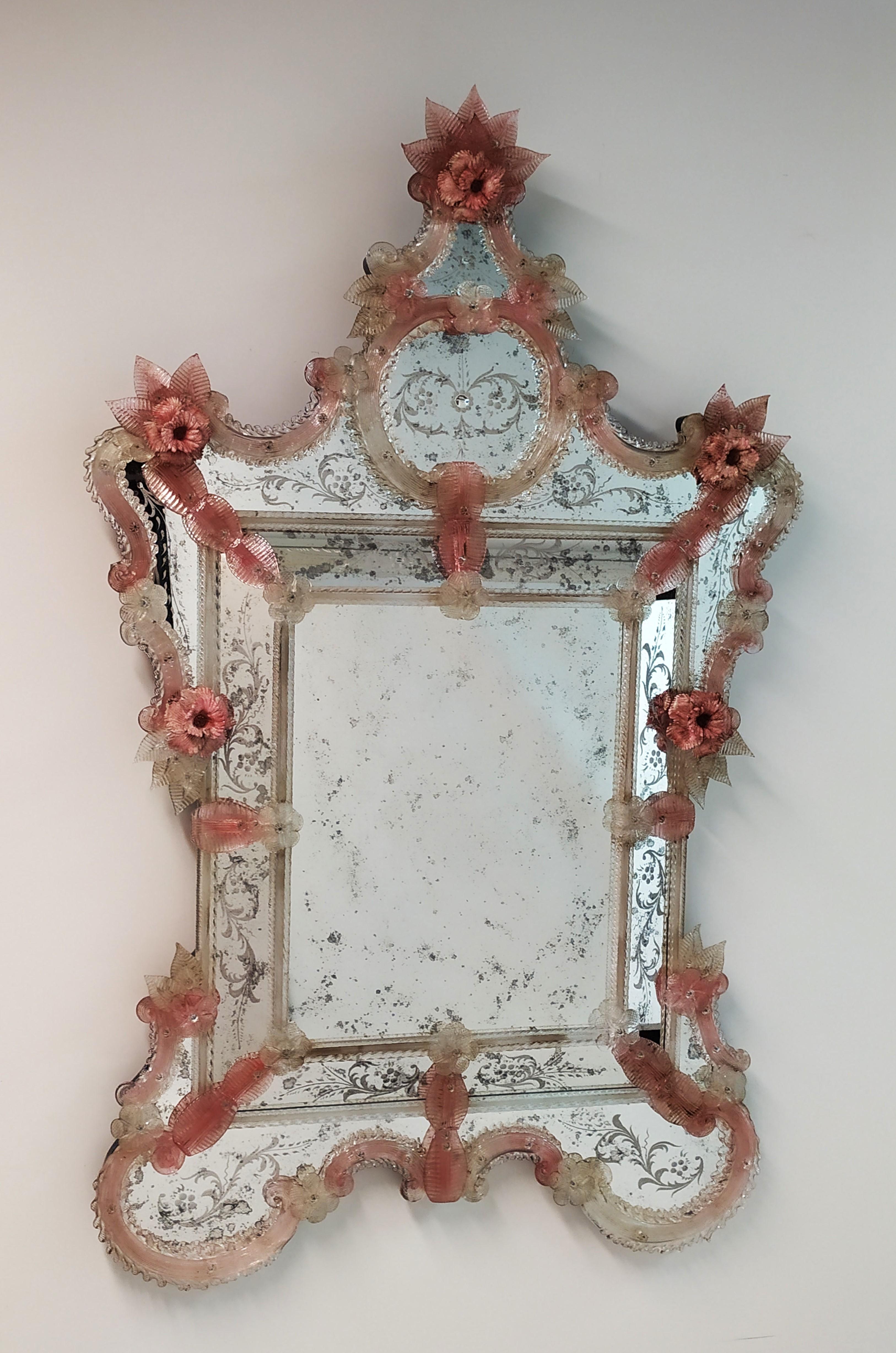 Riproduzione di uno Specchio Veneziano Antico del XX secolo, anticato, inciso e lavorato a mano, con cornice e foglie in colore cristallo e rubino antico , fiori in pasta vitrea di colore rosa in vetro di Murano, realizzato secondo le antiche