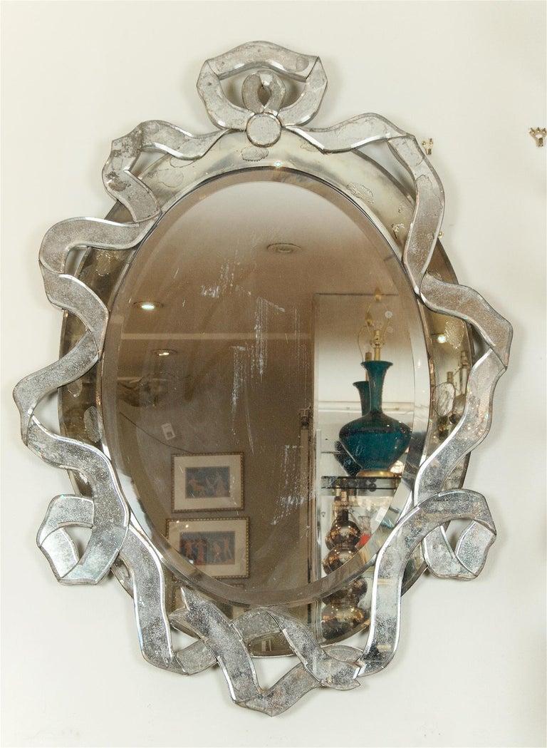Elegant and streamlined Italian mirror, the central oval section framed by a minimally decorated scrollwork or ribbon design composed of individual pieces of antiqued mirror. Mounted on silver painted wood backing.

Glamorous but restrained effect