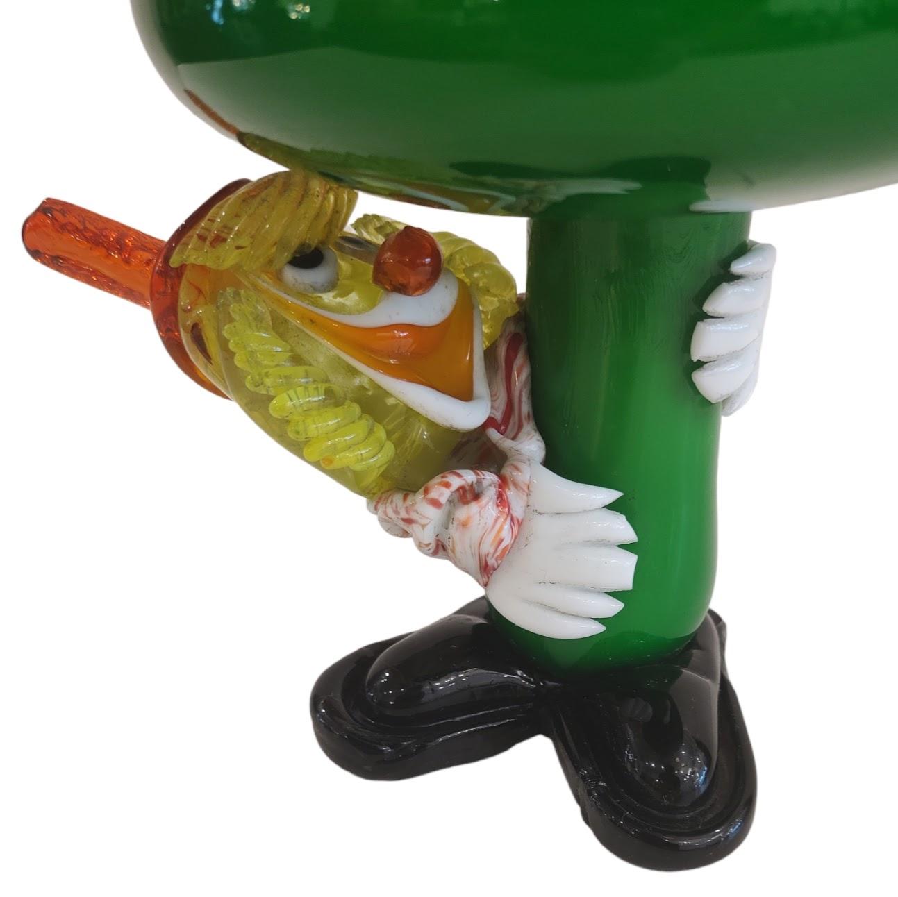 Sous le champignon, le clown vénitien de Murano 
Figurine clown et champignon en verre d'art de Murano, Italie. Le clown s'accroche à la tige du champignon et regarde autour de lui ; il est fait de verre d'art coloré. Il s'agit d'une belle pièce en
