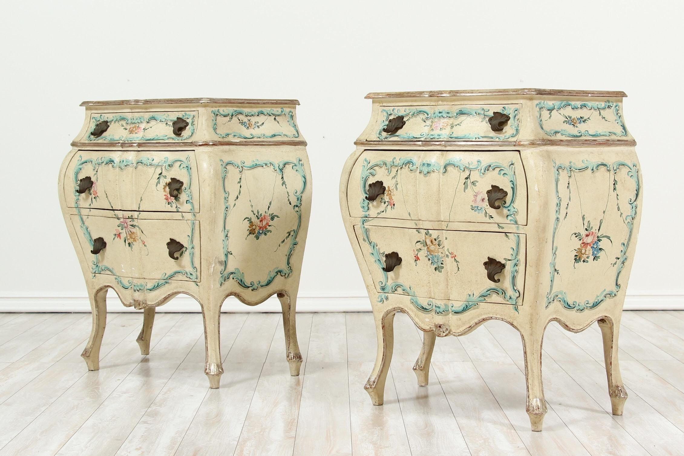 Elegant pair of Italian, 1930s bombe chests or nightstands hand decorated in the Venetian style. These shapely nightstands feature hand painted floral decorations, silver-gilt borders and faux-marble painted tops. Wear to paint finish is consistent