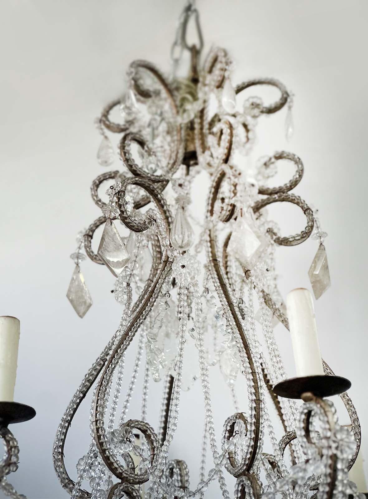 Suspended from an ornate metal frame, the chandelier emanates a timeless elegance that captures the essence of Venetian opulence. Adorned with handcrafted crystal beading, the chandelier exudes a luxurious charm. Each bead is carefully shaped and