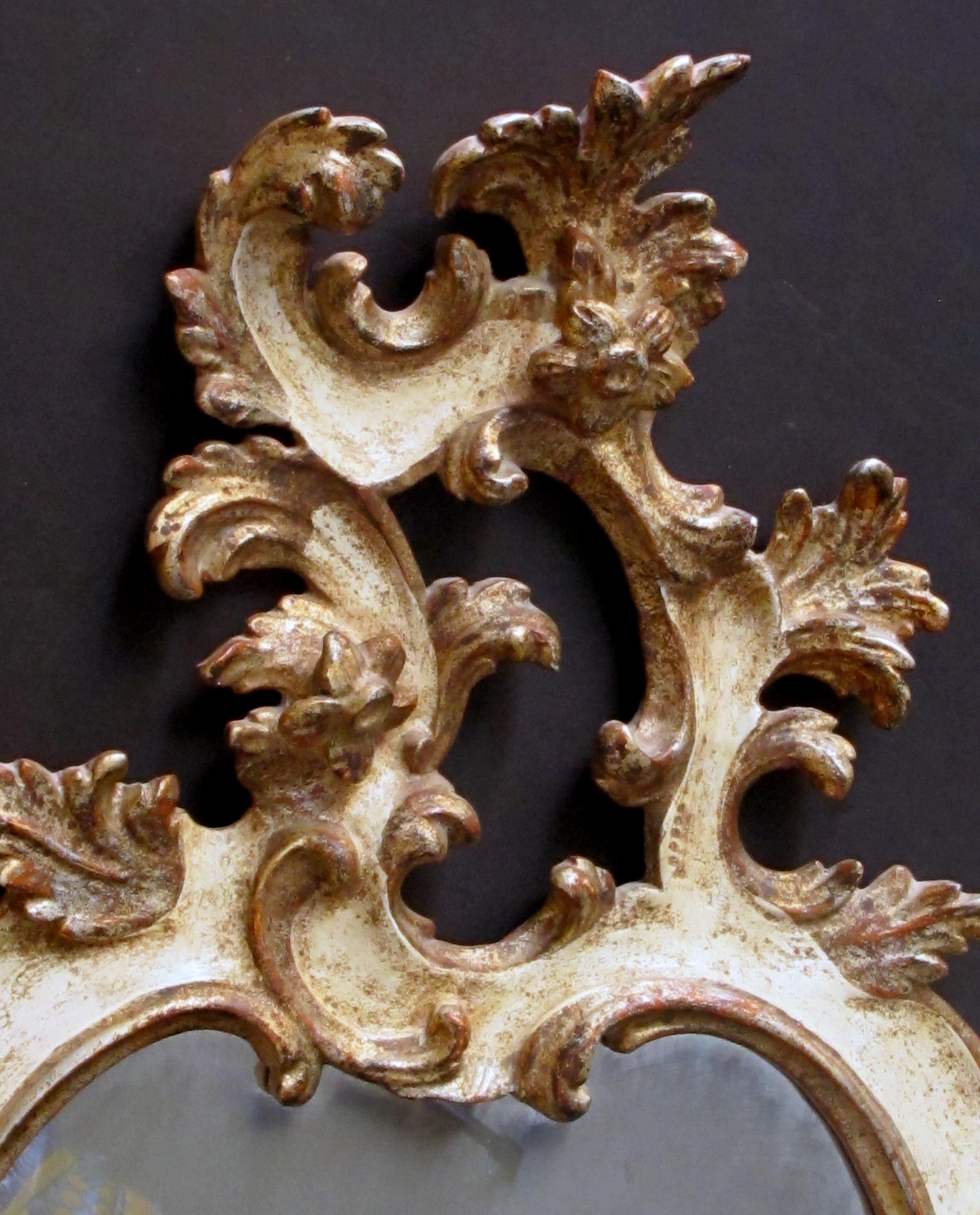 A fanciful Venetian Rococo Revival ivory painted and parcel-gilt cartouche-shaped mirror; the exuberantly carved mirror with openwork asymmetrical crest above a cartouche-shaped body all adorned with foliate and rocaille carving.