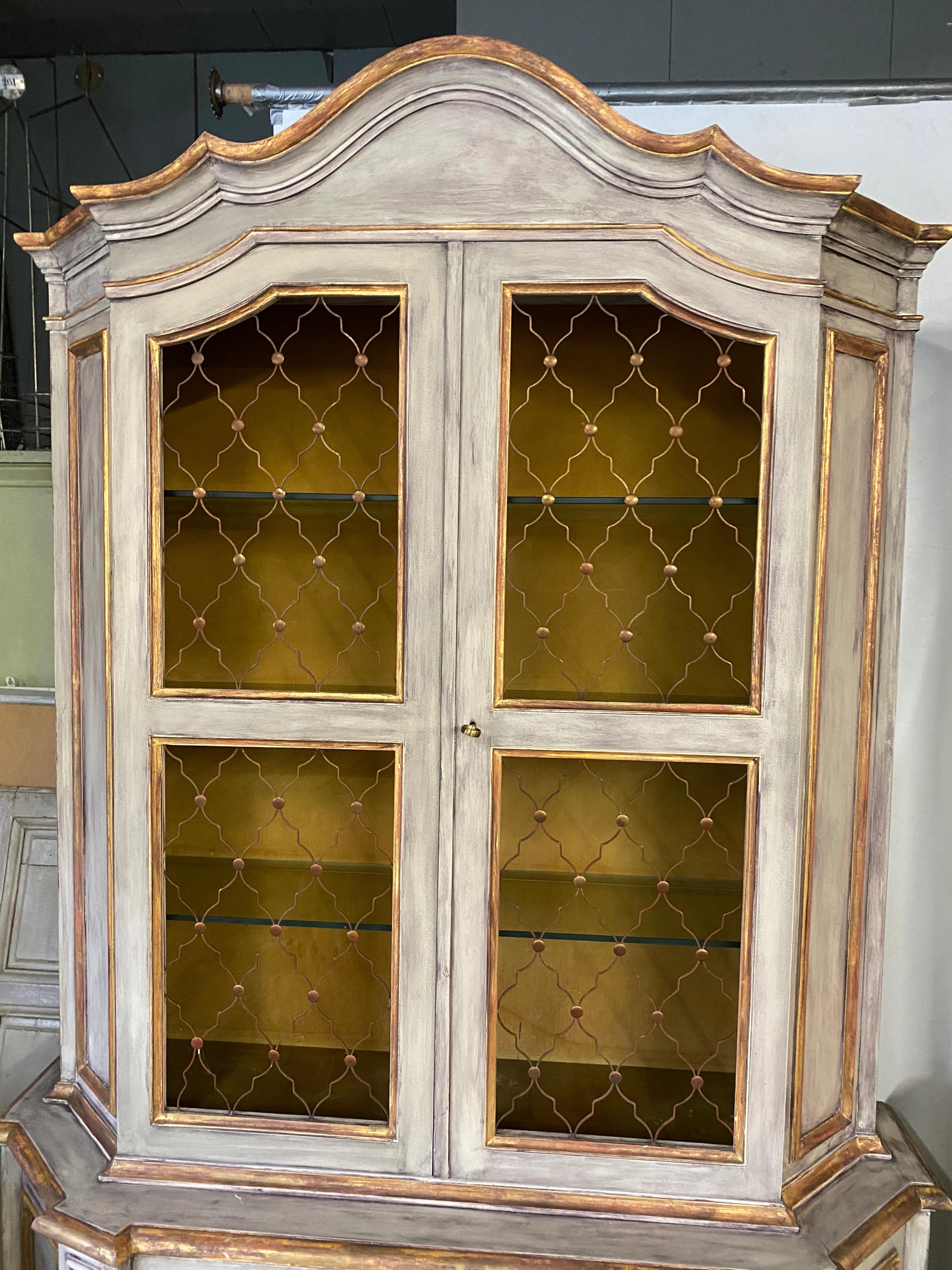Venetian style cabinets have four (three glass) open shelves behind a pair of doors paneled with copper-colored screens above and two shelves below behind solid paneled doors. The pediment is in the Baroque Venetian style. Interiors above are lined
