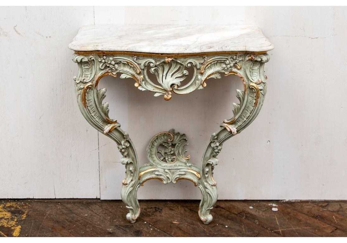 A classic shaped Venetian baroque form wall console carved and painted an antique type pale green with gilt details. Broad foliate scrolled frame with open crest ans cartouche form terminal, With conforming white marble top with carved edge.
