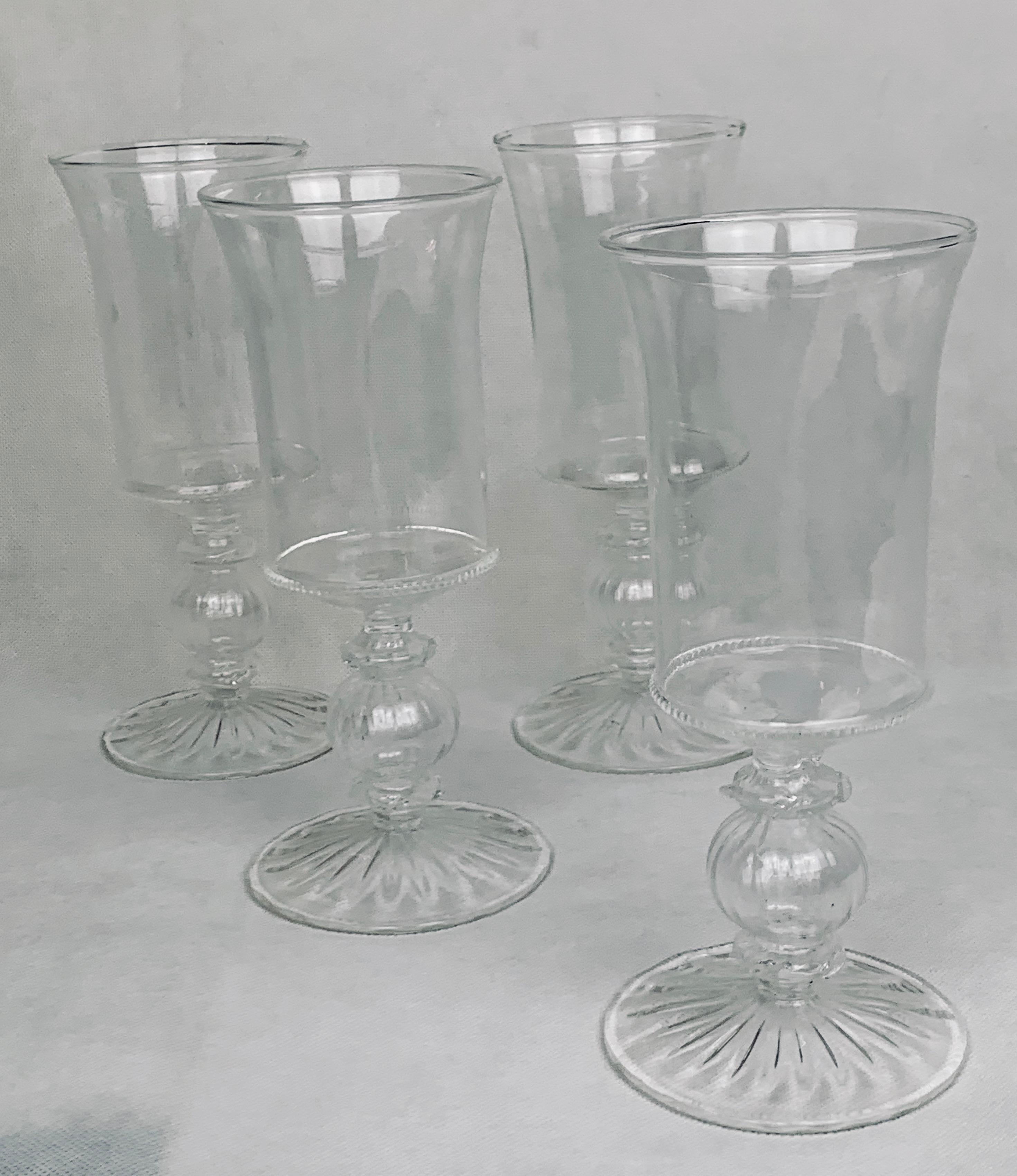 Set of four clear hand blown Venetian style glasses. The bowl with a flared mouth sits on top of an optic ball and a fluted foot. This set of stems have never been used.  This shape is very versatile and can be used for wine, iced tea, beer or