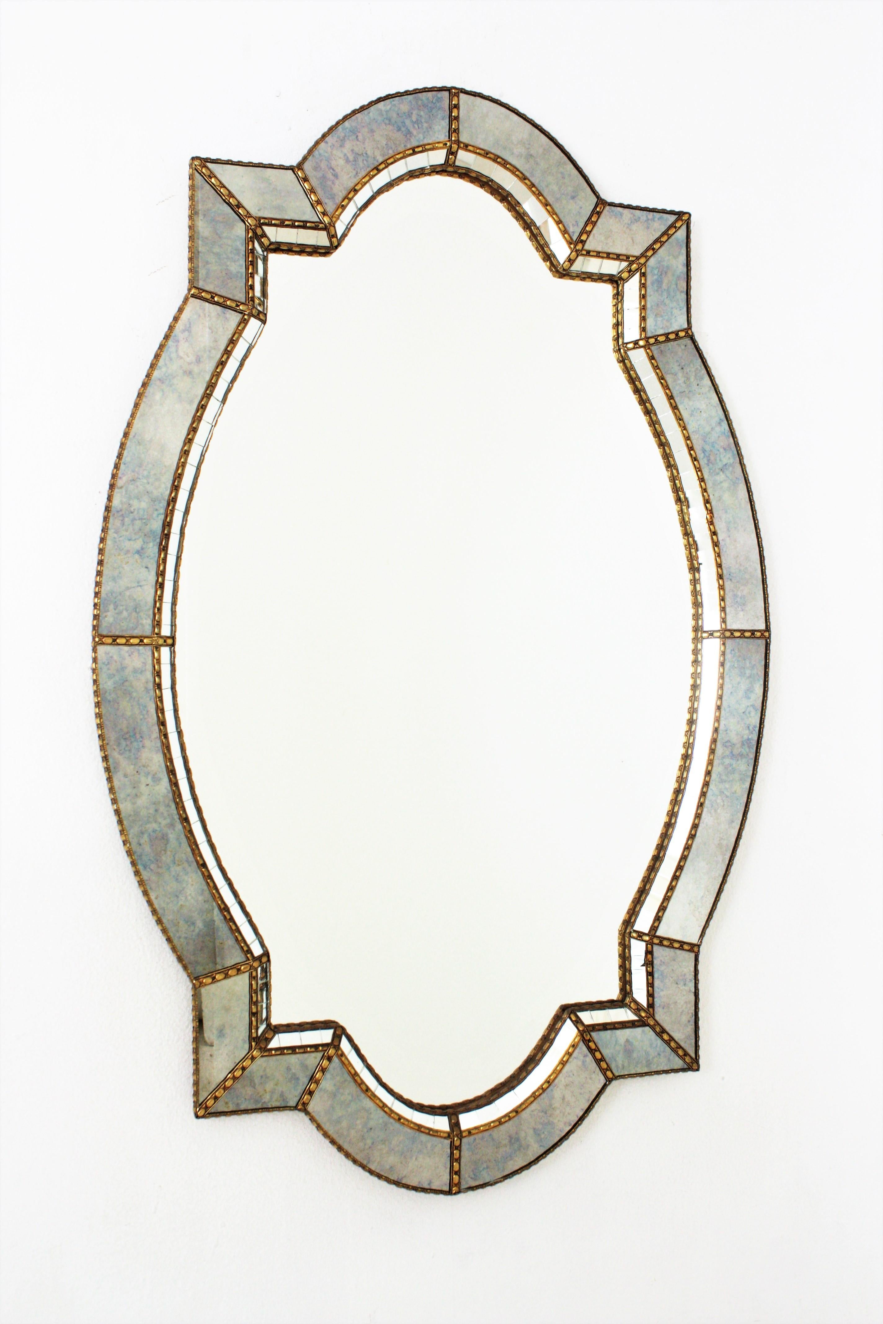 Elegant venetian style Hollywood Regency wall mirror with iridiscent blue glass frame. Spain, 1960s.
This glamorous mirror featuring a double layered elongated quatrefoil mirror. The frame is made of brass with two layers of decorative paneled