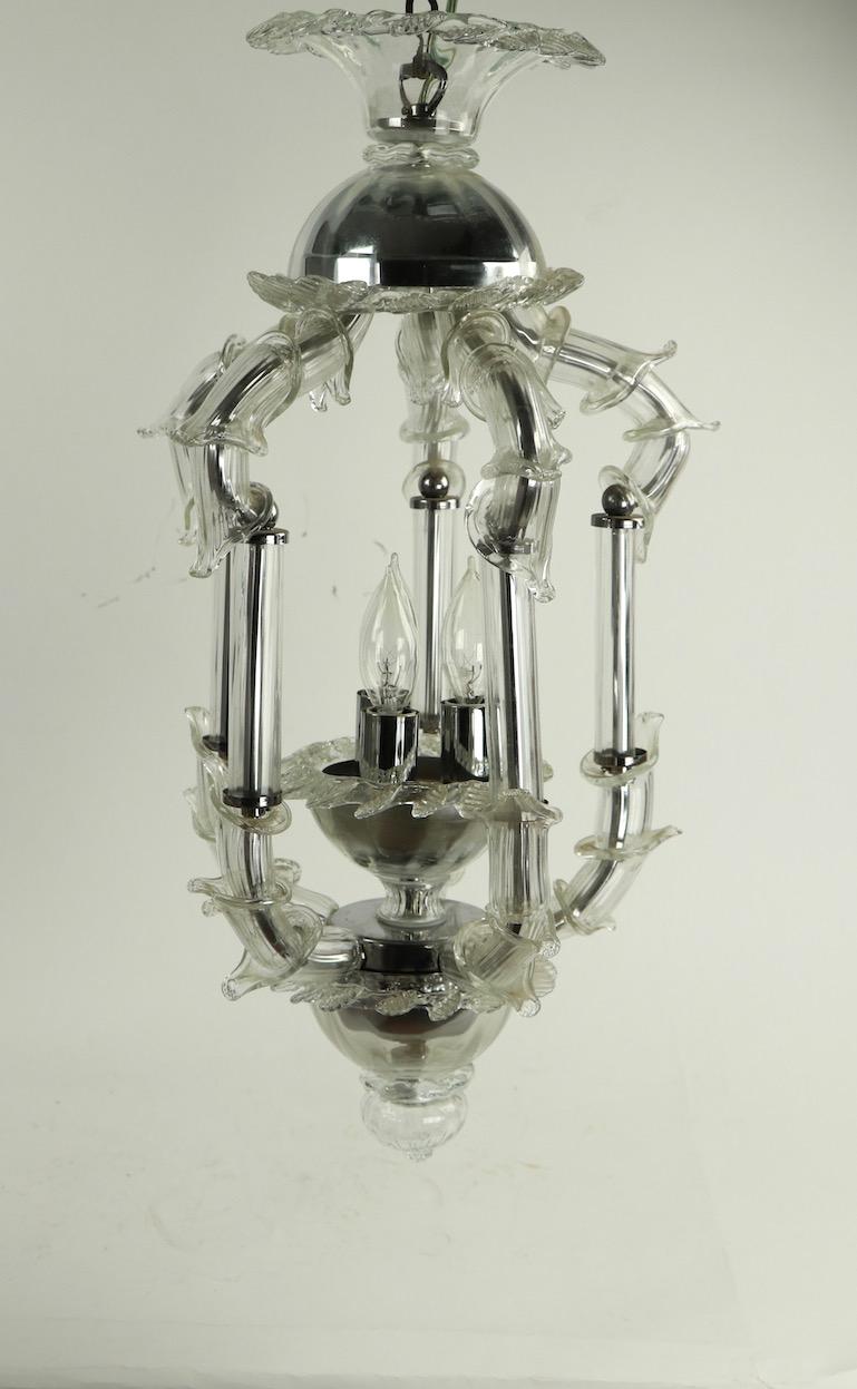 Luminaire chic en verre de Murano de l'école vénitienne, de style Hollywood Regency, comportant cinq bras en verre tubulaire avec des garnitures chromées, une couronne et une base en verre. L'intérieur peut accueillir trois ampoules à bougie