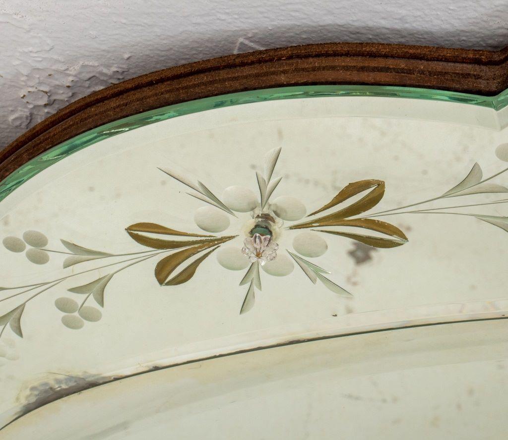 Miroir mural ovale de style vénitien avec verre biseauté et motifs de feuilles et de fleurs gravés.

Concessionnaire : S138XX