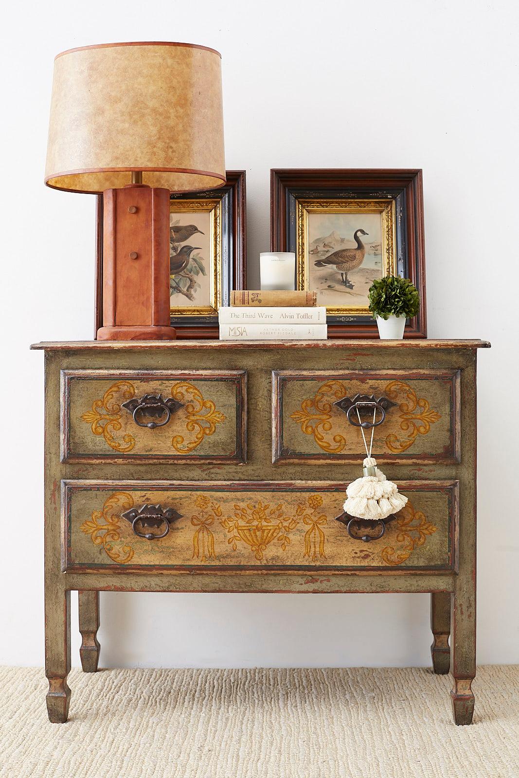 Distinctive painted three drawer commode or chest of drawers featuring a hand painted lacquer finish. Decorated in the Italian neoclassical taste on three sides and top with acanthus, urn and floral motifs. Constructed from hardwood with rustic iron
