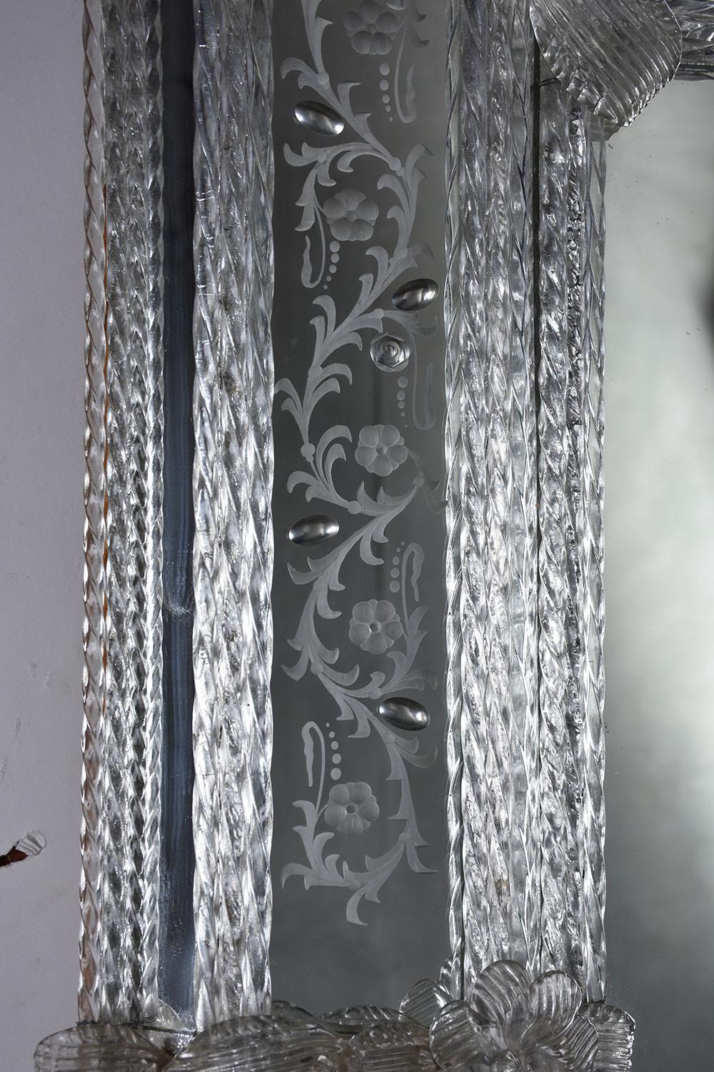 This 1980s Venetian wall mirror. The rectangular mirror simple structure is masterfully decorated with the use of hand-engraved motifs and Murano glass flower-shaped decorations in crystal color. The exquisite texture created gives the mirror a