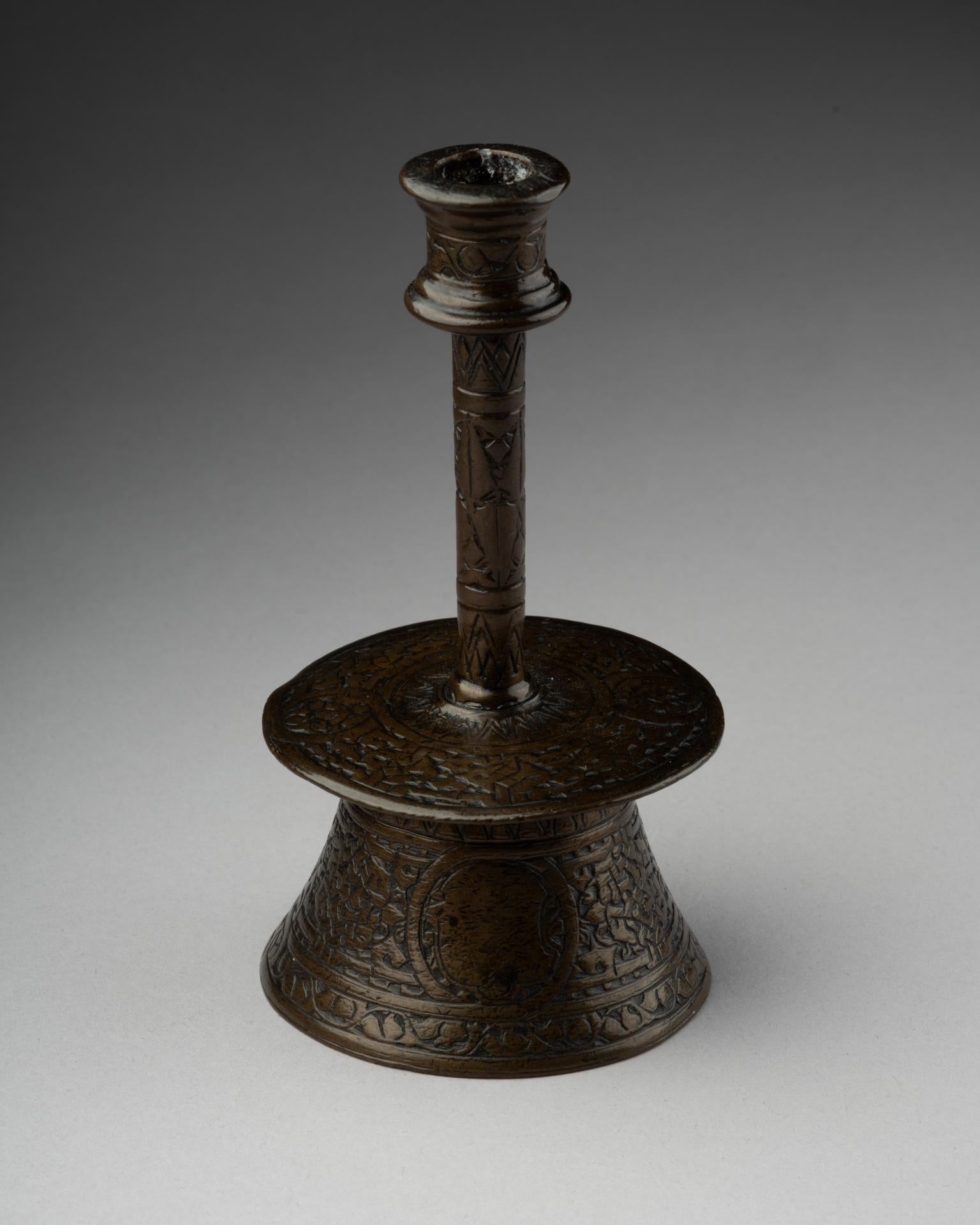  Candeliere veneto-saraceno
Bronzo inciso
XV secolo
12,5 x 6,2 cm
Questo raro candeliere è un esempio di squisita fattura, caratterizzato da una base a campana con un piede svasato ornato da intricati motivi incisi. La decorazione consiste in