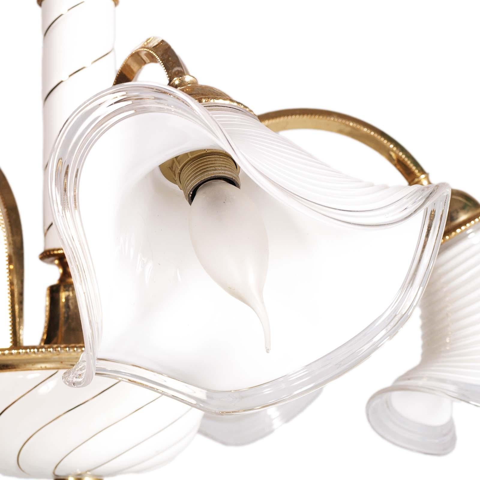 Elégant lustre Murano des années 70, 5 lumières, métal doré verre laiteux, avec système électrique révisé et prêt à être utilisé.
Le design est très élégant avec le verre laiteux transparent bordé de fil d'or pur, et les parties métalliques dorées