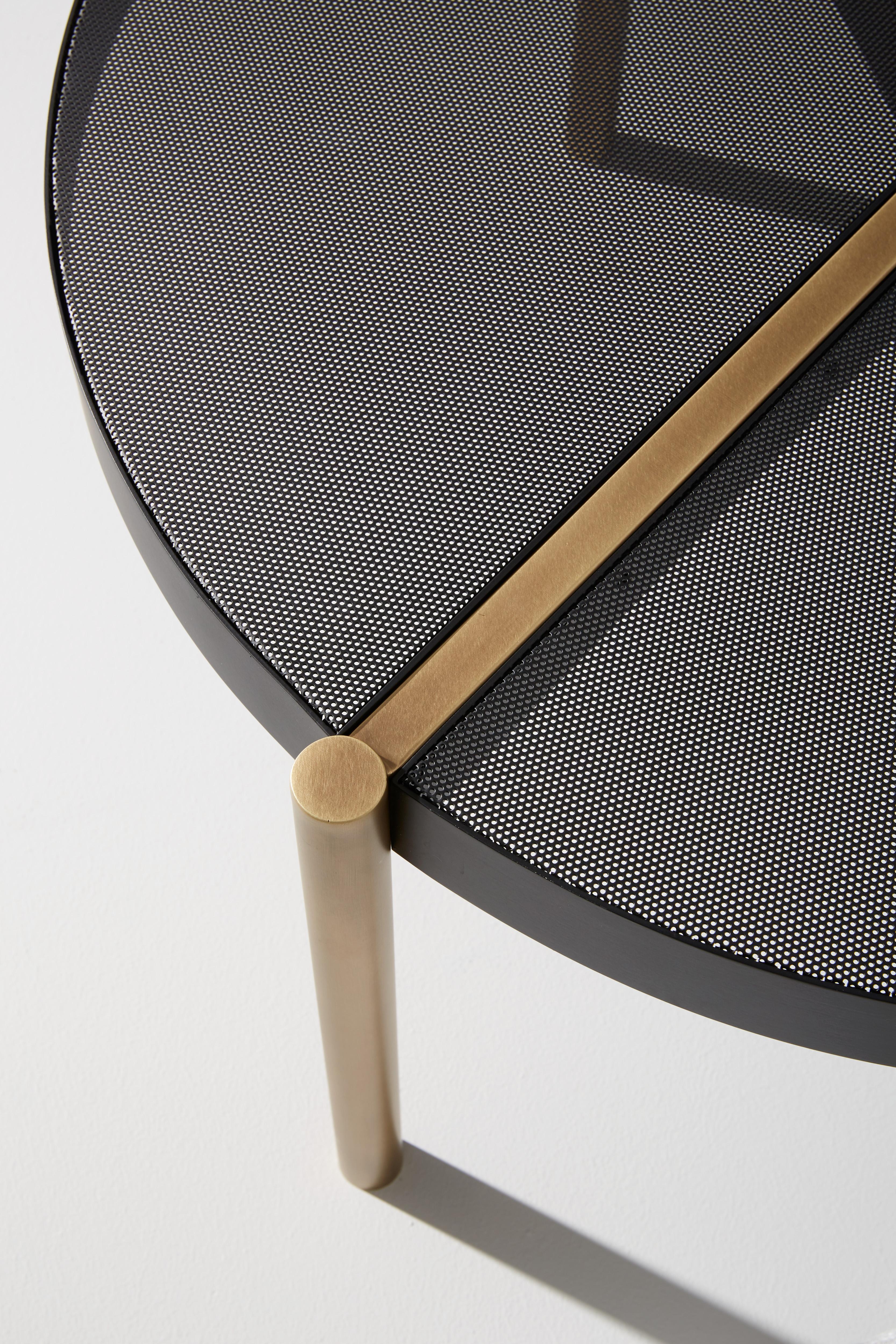 Table basse composée d'une structure en laiton bruni clair et d'un plateau en métal perforé noir mat.
        