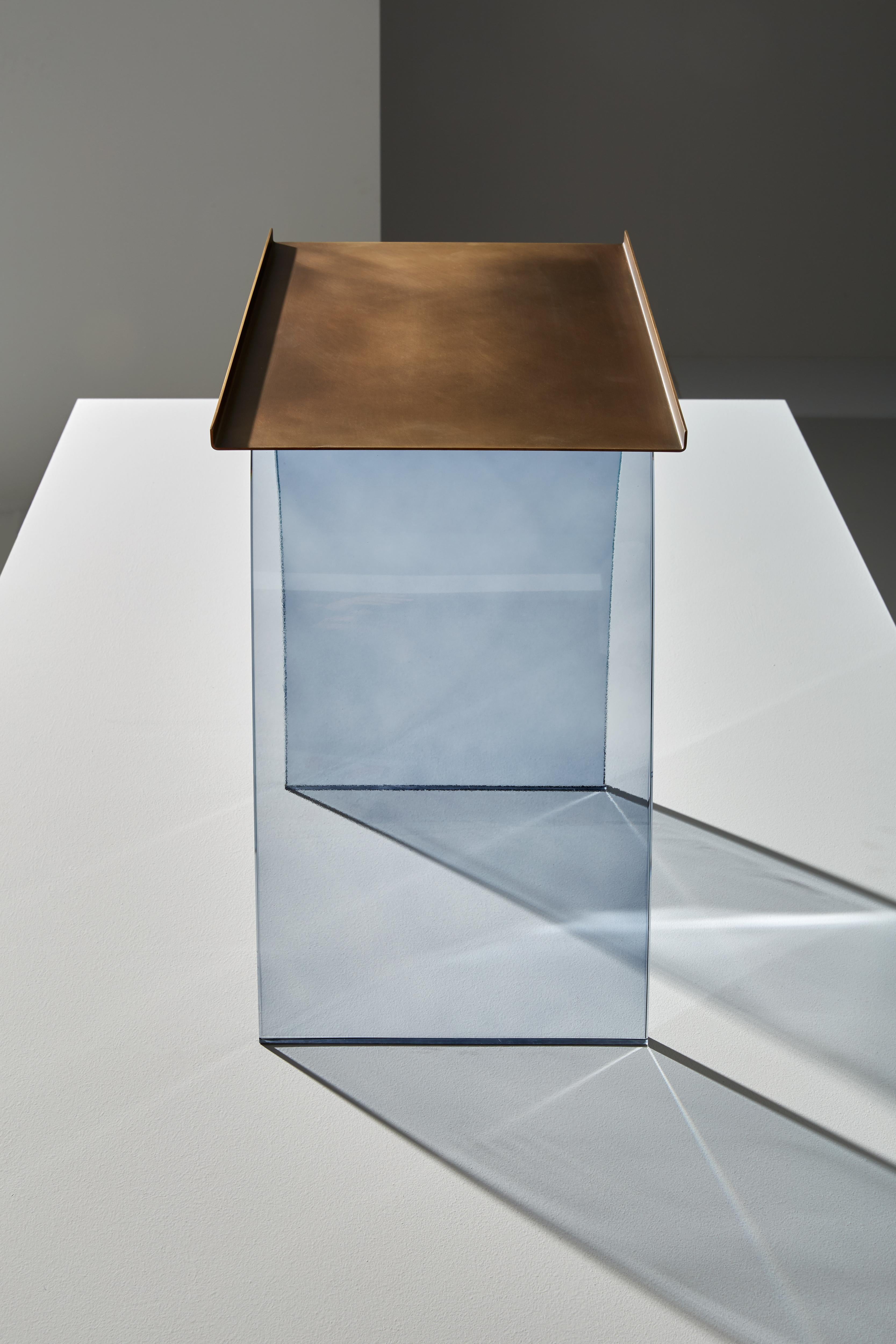 Table basse composée d'une structure porteuse en verre gris fumée incurvé. Dessus en laiton bruni clair.
     