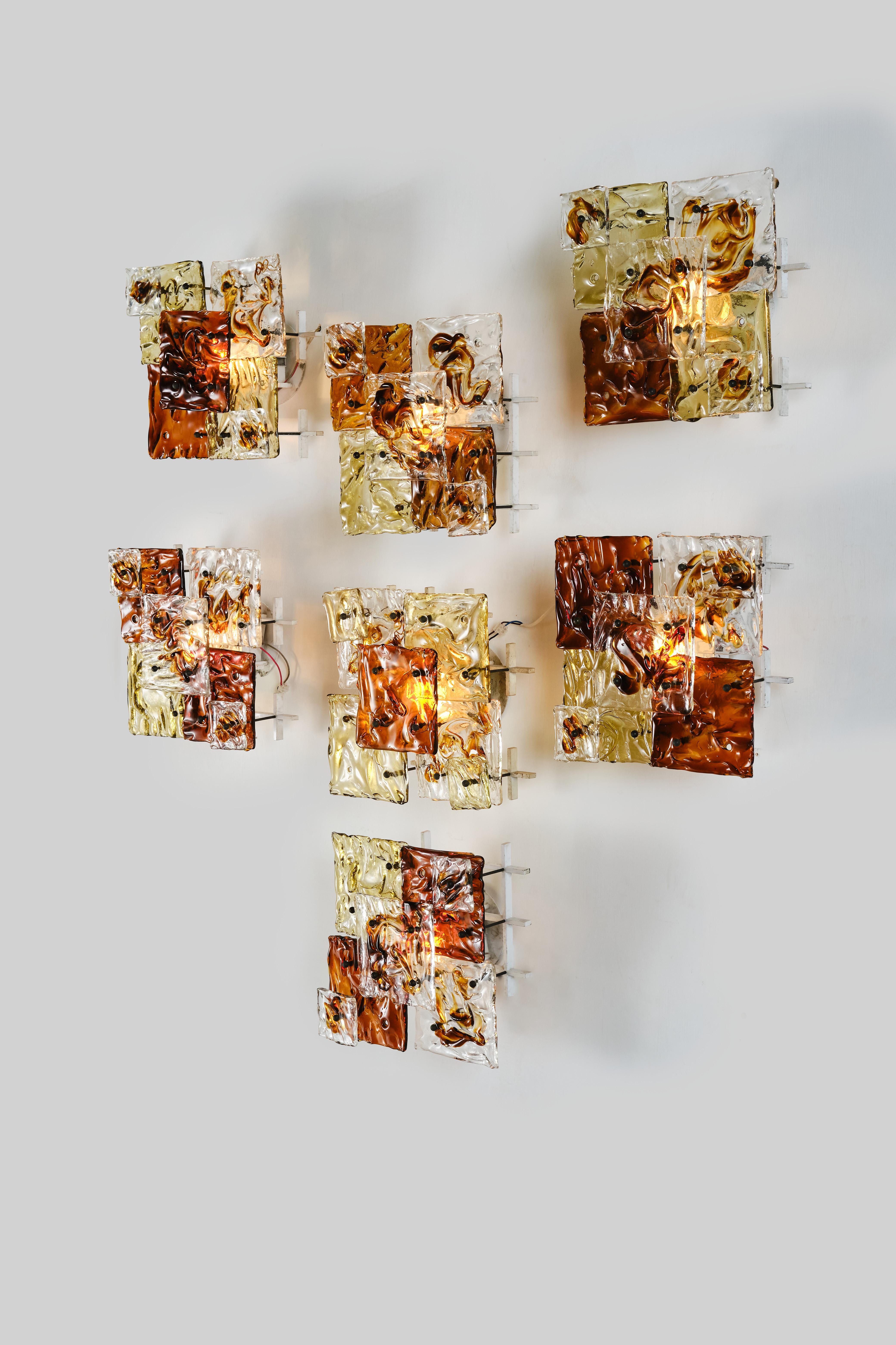 Set of seven incredible wall lights designed by Toni Zuccheri and produced by Venini Murano, model Patchwork.
These beautiful glass handmade sconces are a true work of art thanks to its hot-worked transparent glass, painted metal frame and brass