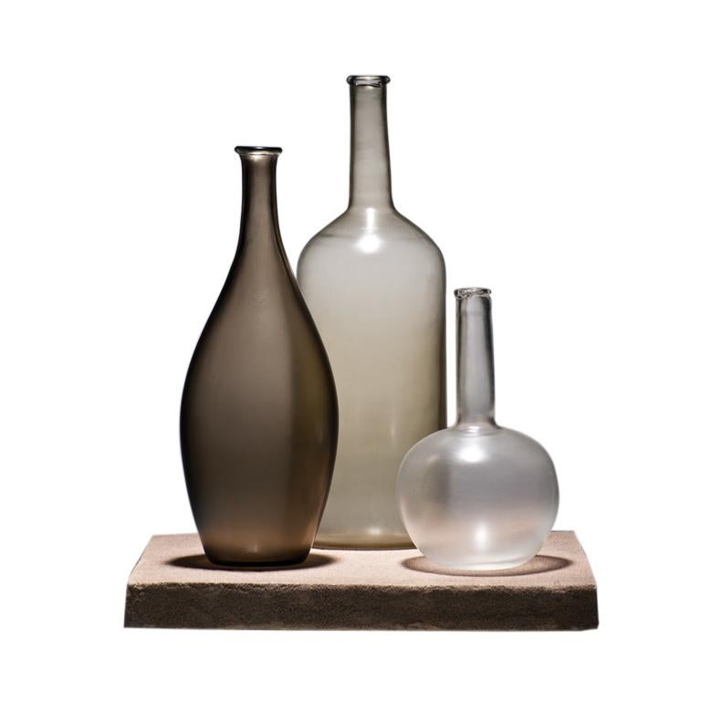 Alla Morandi glass bottles sculptures, designed by Matteo Thun and manufactured by Venini, feature bottles in blown handmade glass, then veiled and cut on the mill. Base in Santa Fiore stone. Limited edition of 30 pieces plus 5 for each. Indoor use