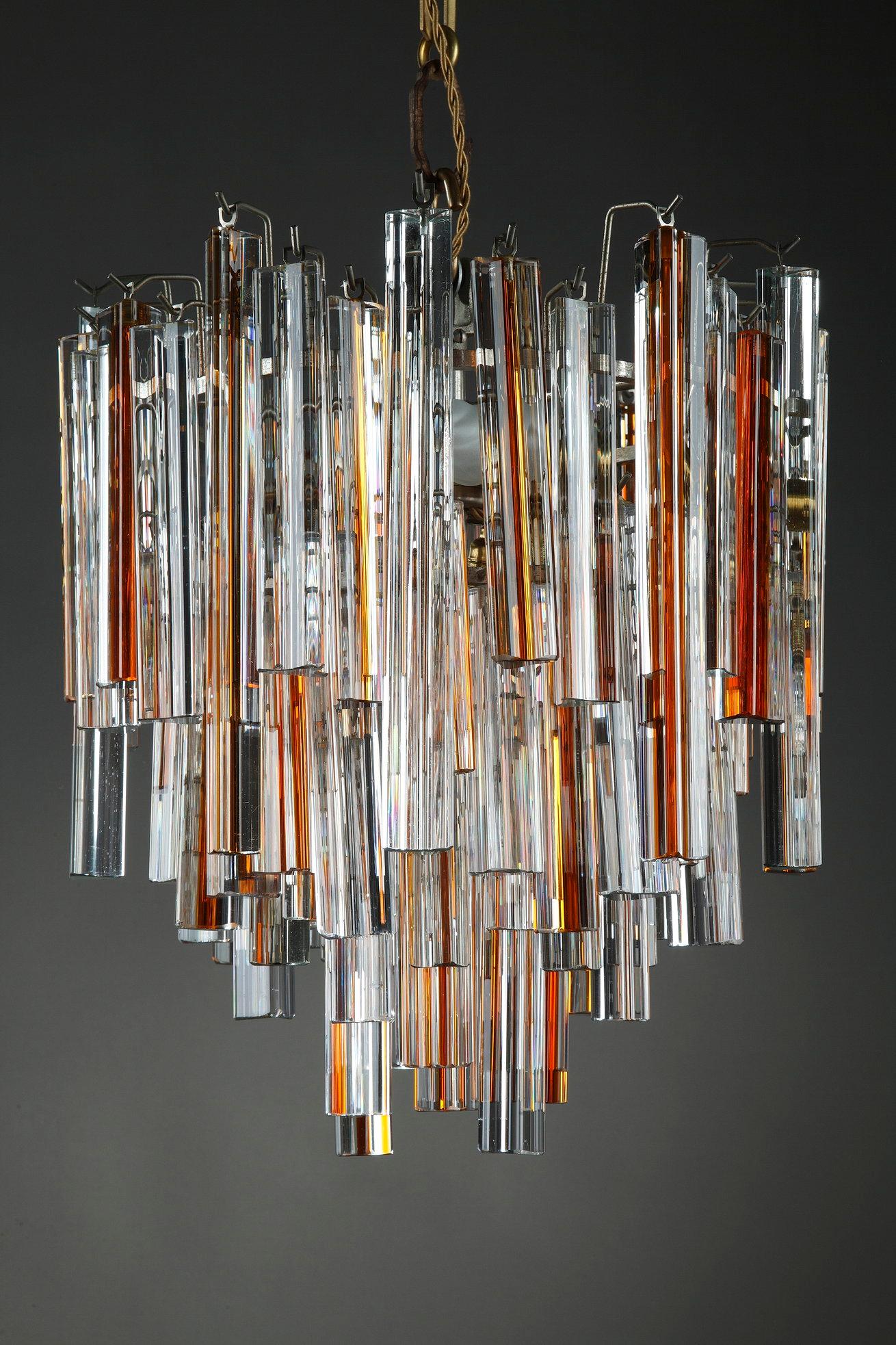 Inverted pyramidal chandelier composed of Murano glass pendants of triangular section translucent and with orange nets. The pendants are beveled at their ends. The central frame is made of chromed metal. The chandelier works with 4 lightbulbs.