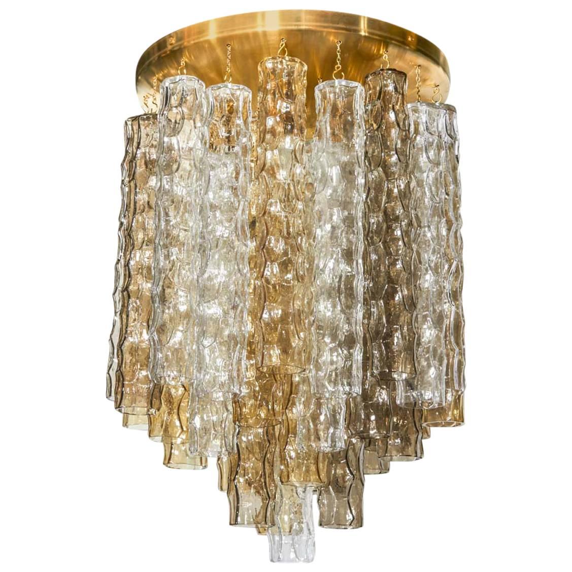 Mid-Century Modern Hollywood Regency chandelier comprised of three tiers of hand blown Murano glass pendants with bamboo texture and design. The glass pendants come in alternating colors (smoked grey, amber, and clear). Features a large brass dome