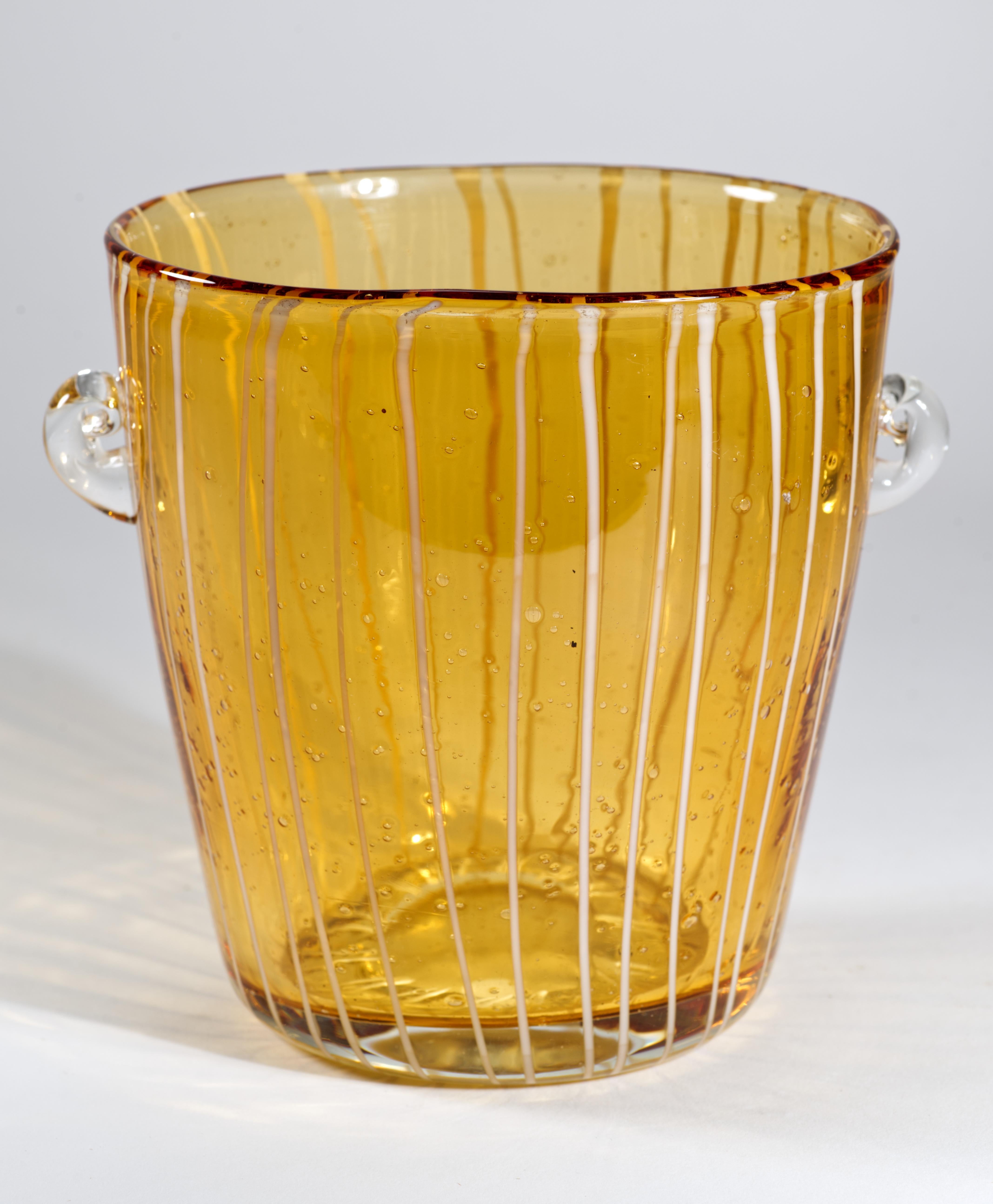  Modernist vintage ice bucket has abstract geometric decor of fused white glass on transparent amber colored glass with controlled bubbles effect. The piece has two small rounded handles that are done in clear glass and attached separately. 

While