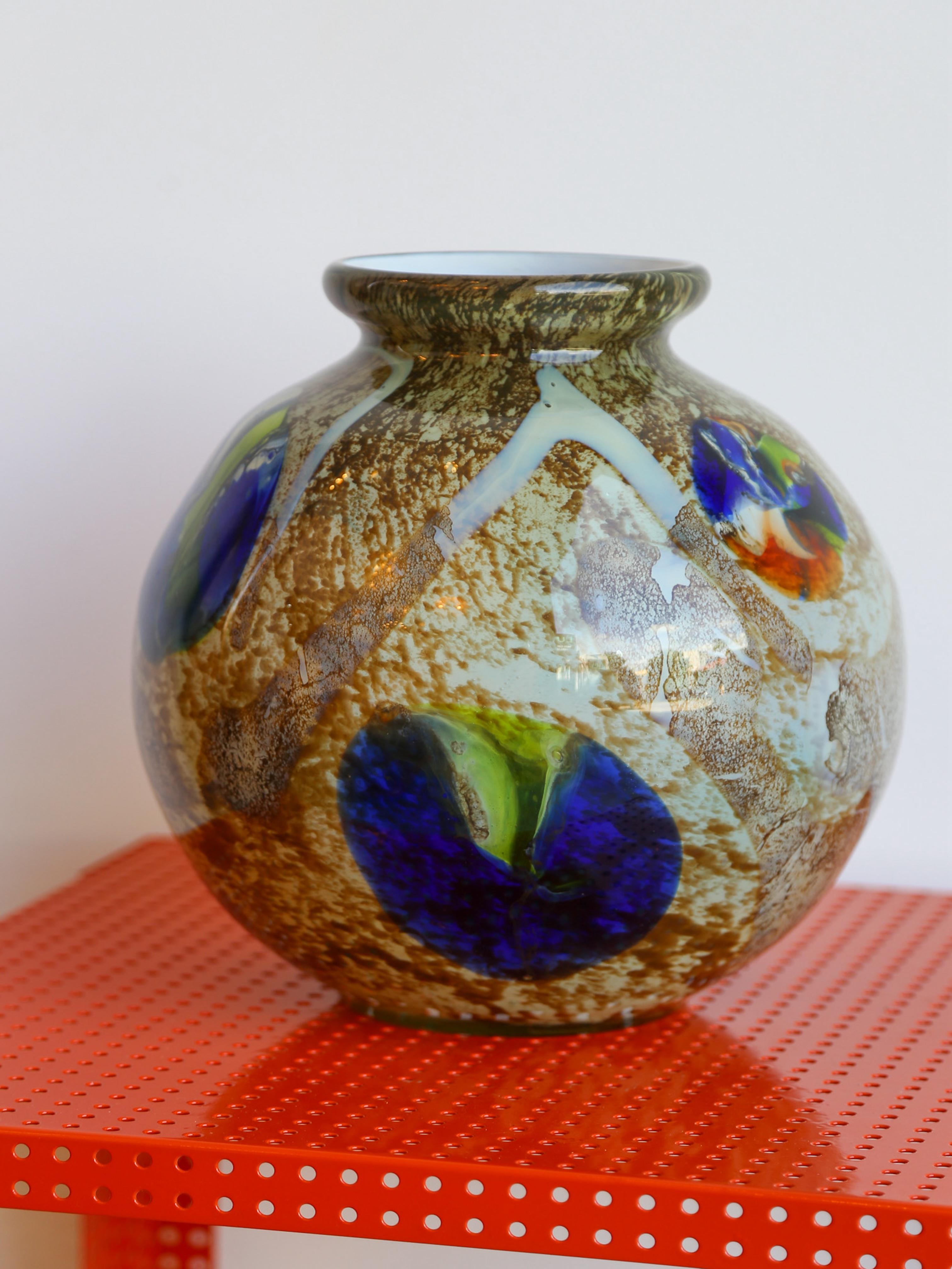 Vaso firmato Venini 
Una vera e propria testimonianza dell'artigianato italiano. Soffiato a mano da abili artigiani, questo pezzo unico presenta un'ipnotica miscela di toni della terra, blu profondi e verdi vibranti, che creano un effetto visivo