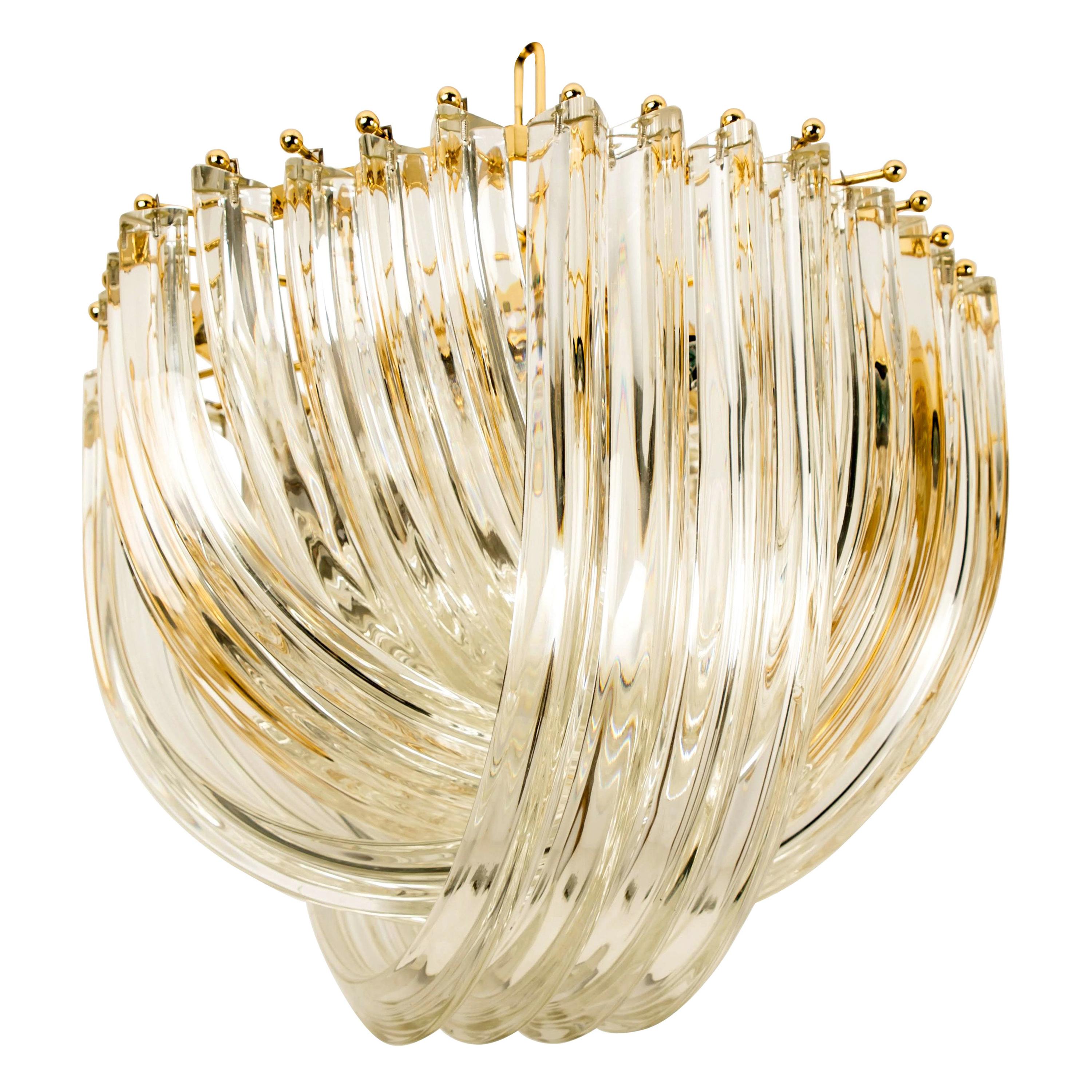 A pair impressive light fixtures by Venini, Italy, manufactured in circa 1970 (late 1960s-early 1970s). A handmade and high quality piece. Large curved crystal Murano glasses in different length mounted on a gold-plated brass frame. The crystals are
