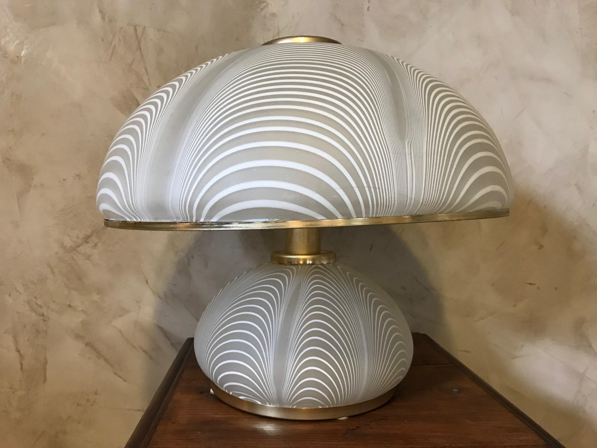Exceptional Murano glass table lamp designed by Paolo Venini in the 1970s.
This lamp has a mushroom shape and made of mouth-blown white and clear striped art glass with very fine brass elements. The lampshade is also rimmed with brass.
There are