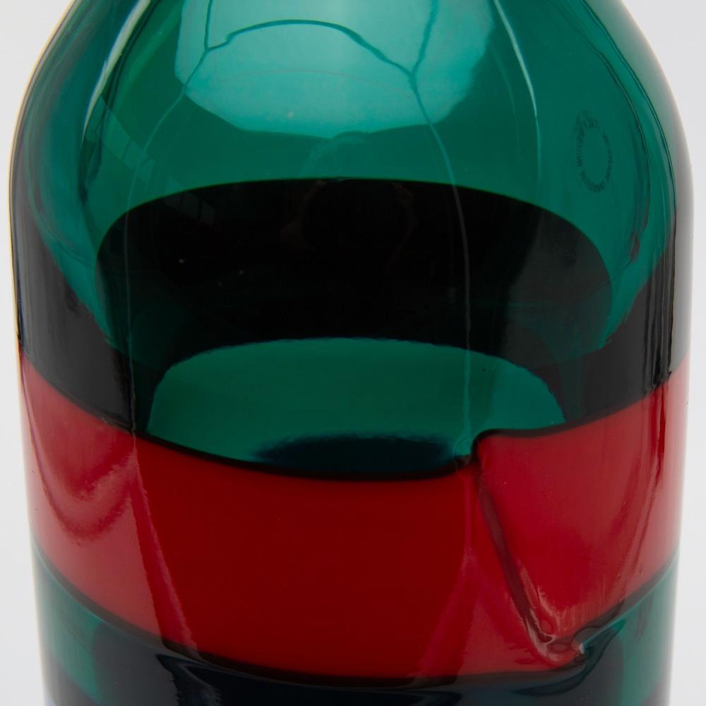 A beautiful and large bottle with stopper designed by Fulvio Bianconi for Venini Murano in Italy.
The color of the body is a strong green with 3 vertical applied glass bands, two red ones and one blue.
The stopper has a same blue 