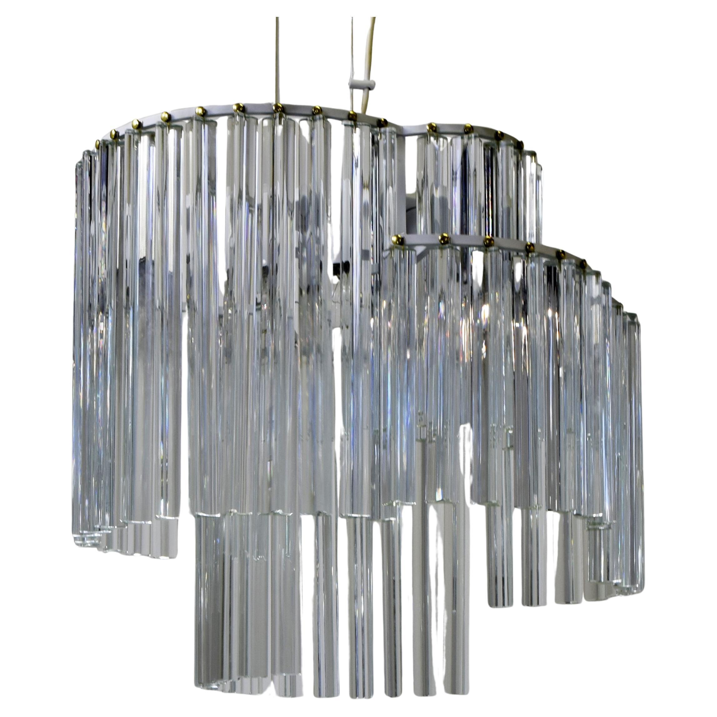 Cet élégant lustre présente une structure multicouche avec des éléments en verre de Murano dans le style emblématique de Venini. Les pendentifs sont formés par de longues tiges trilobées de verre clair, façonnées et légèrement prismatiques, qui