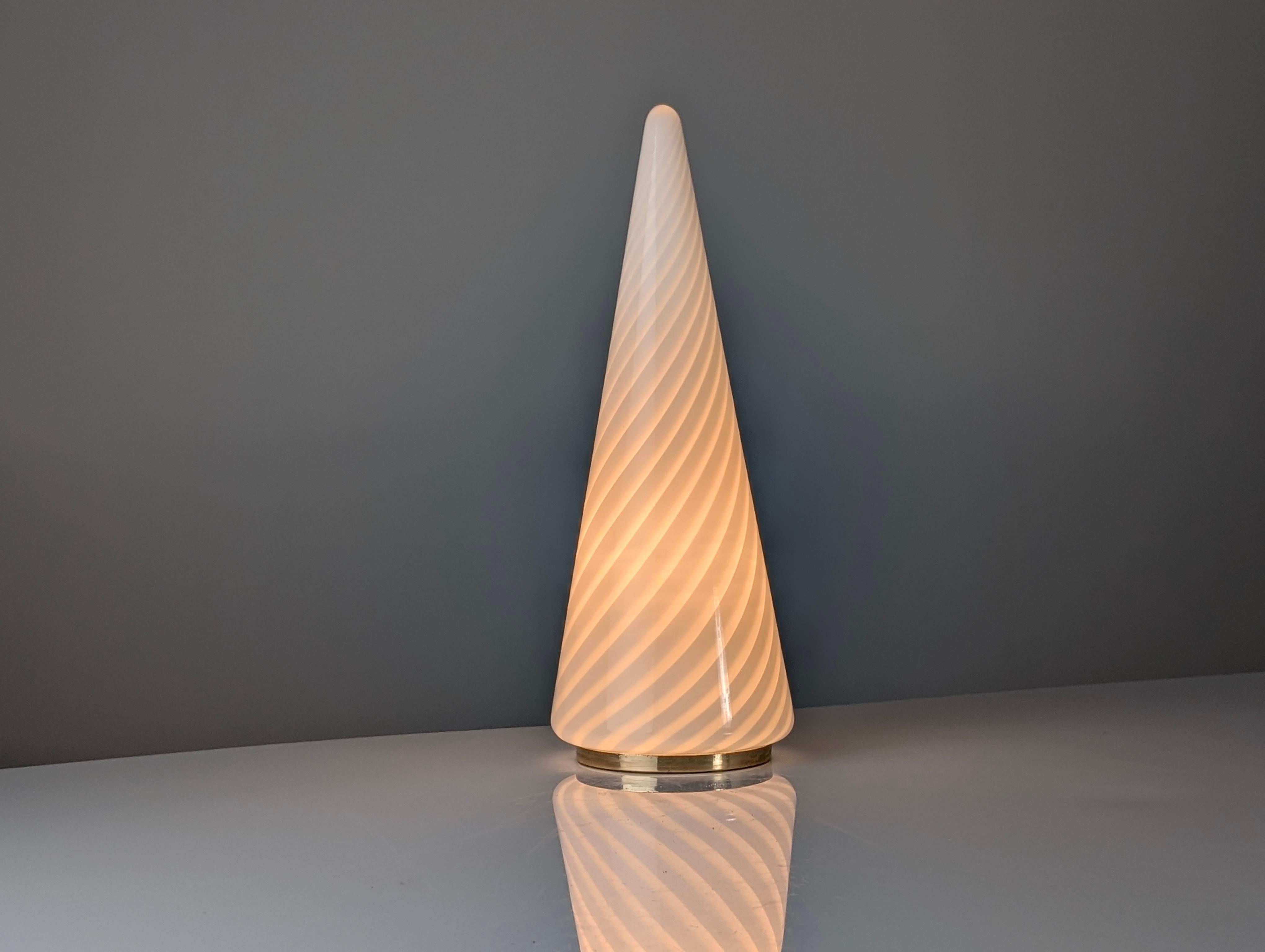 Cette lampe de table en verre de Murano, généralement associée à la verrerie Venini, est d'une grande beauté et d'une grande modernité. La forme conique est caractérisée par un motif interne en spirale, ou tortiglione, réalisé en verre lattimo
