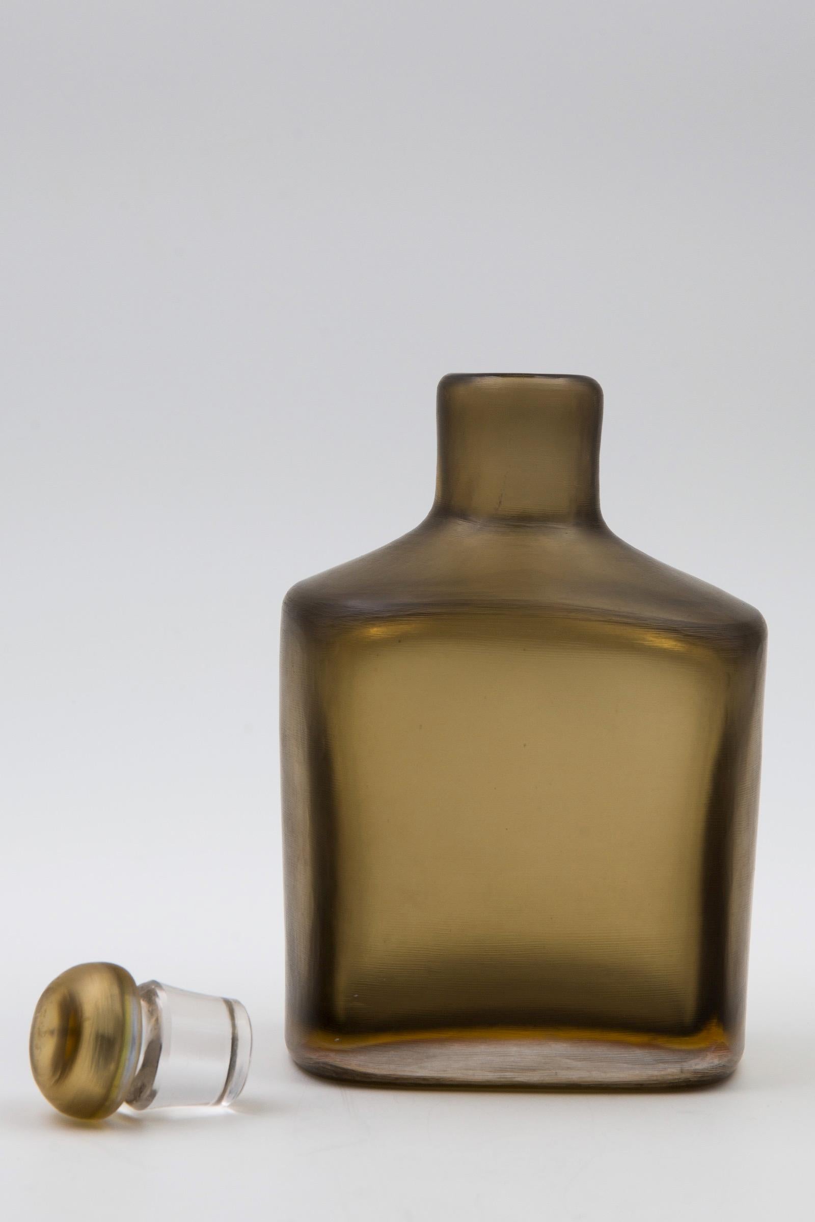 Bottle with stopper in bronze colored pesante glass with a thin layer of yellow glass

The item is finished with horizontal light grinding over the whole surface. This technique has been called by Venini inciso which means incisions in Italian