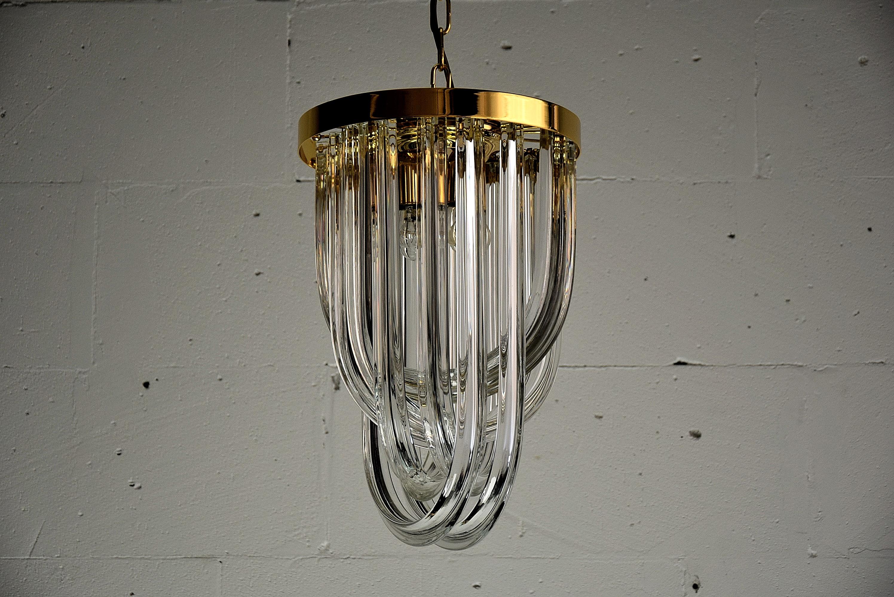 A stylish and classy Italian Hollywood Regency pendant Venini light, circa 1990's. This beauty is made of pairwise curved crystal Murano glasses in different lengths and a gold-plated brass frame. Perfect Condition.

The height of the body without