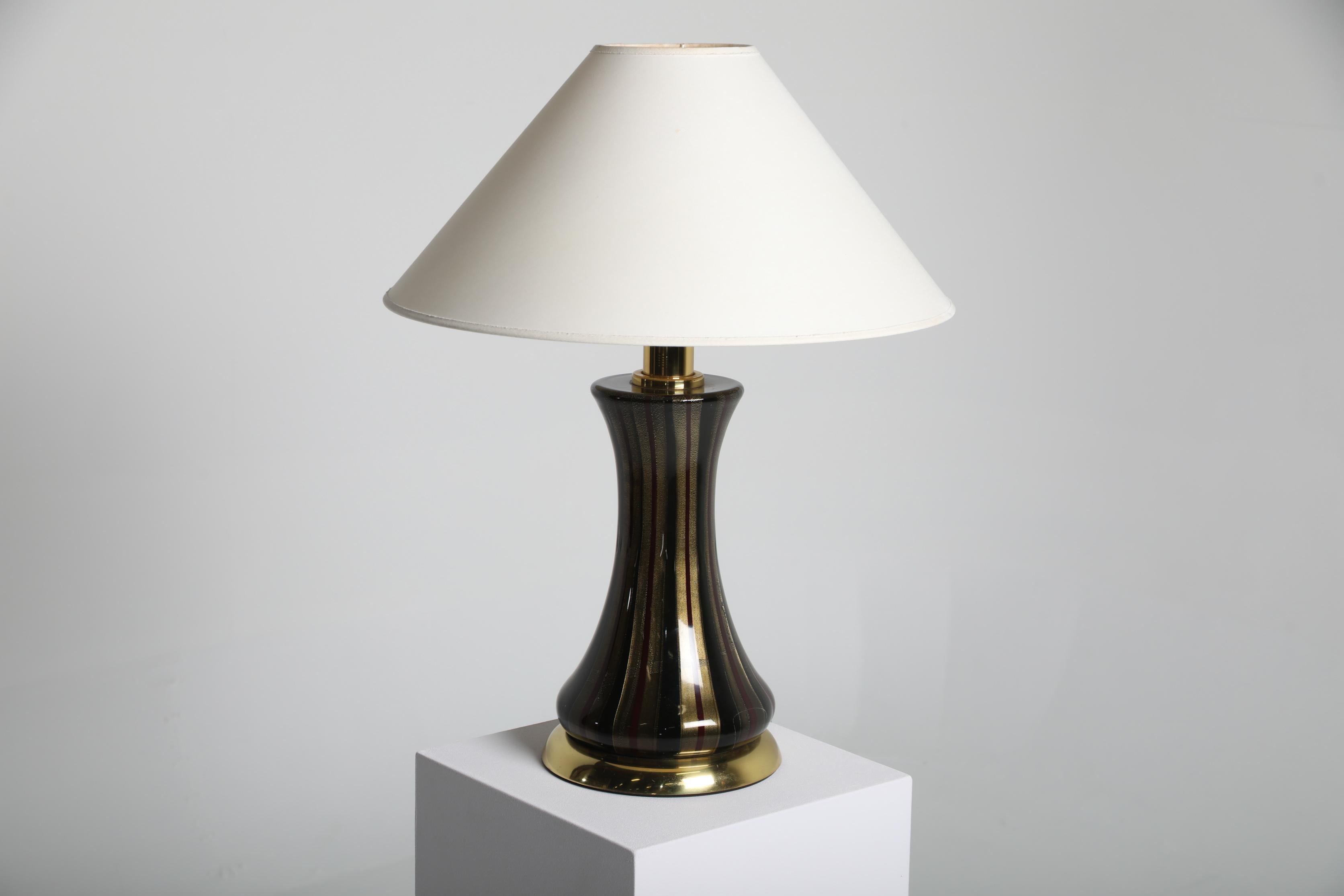 Lampada da tavolo attribuita a Venini, prodotta in Italia negli anni Cinquanta. La lampada presenta una base scultorea in vetro di Murano con dettagli a coste verticali e un piede in ottone, tipico dell'artigianato italiano di metà secolo. Il vetro