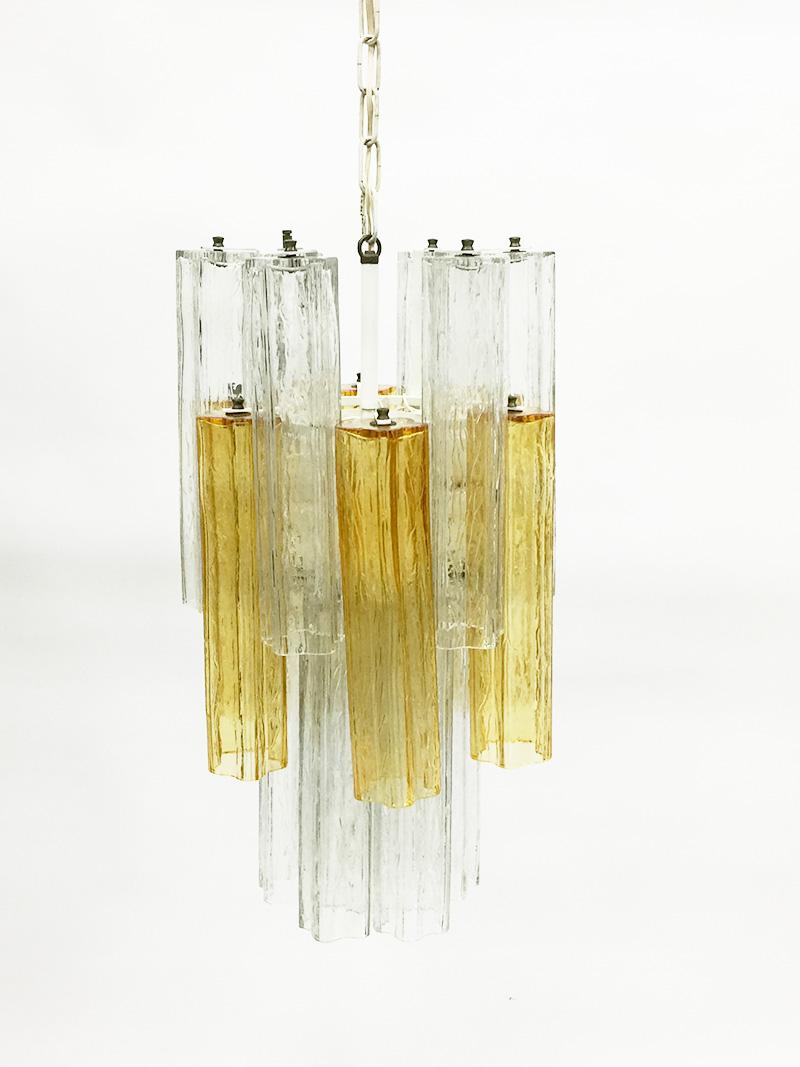 Venini Tronchi chandelier by Toni Zucchini with 2-tone Murano glass tubes

2 tone hand blown in amber yellow and clear textured glass, by Murano, Italy
12 clear glass colored tubes and 6 amber yellow glass colored tubes hanging in a white metal