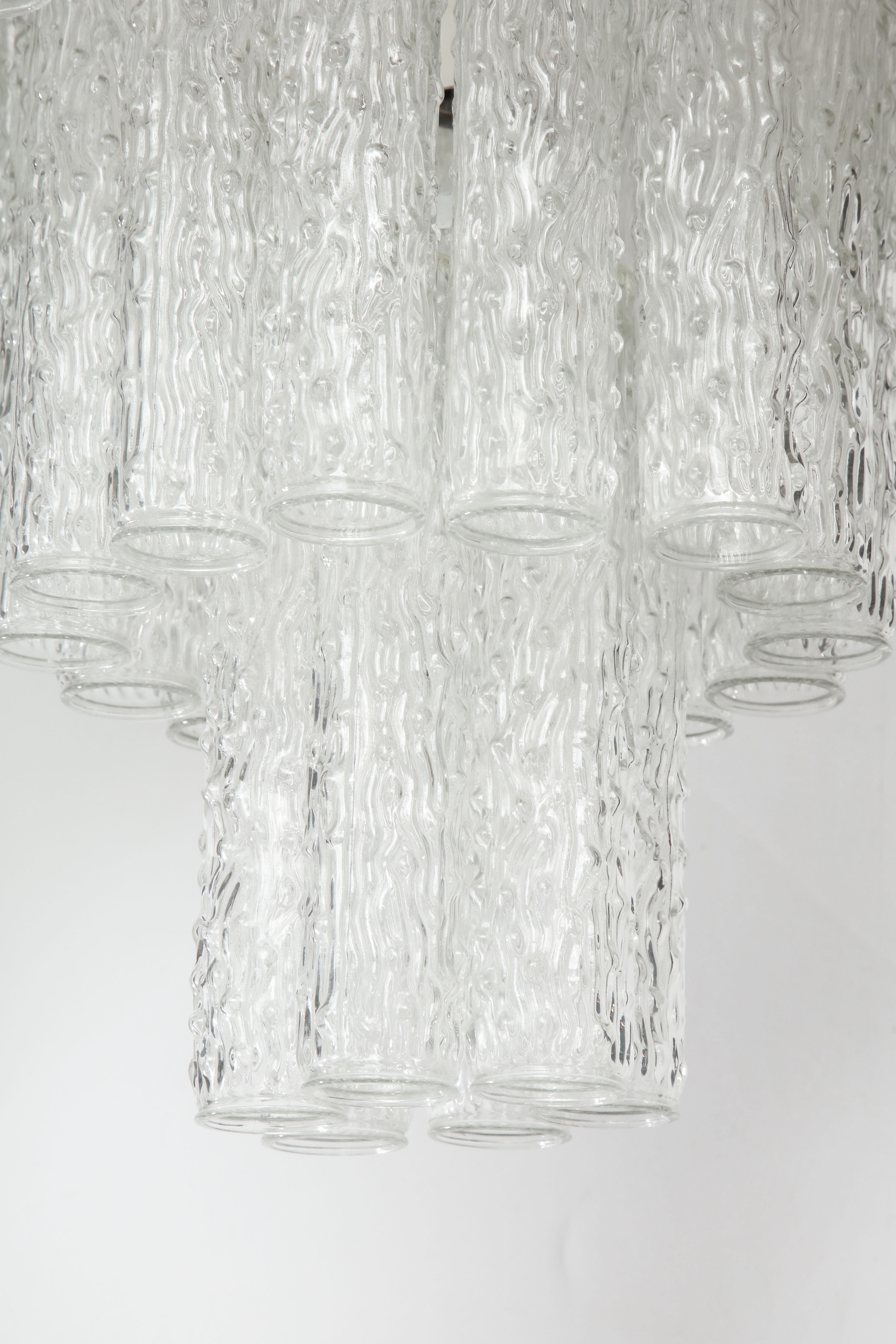 A three-tier chandelier handcrafted in Italy. The piece is made up of a metal frame that supports three tiers of round, clear glass tube crystals. A beautiful way to light up a room!