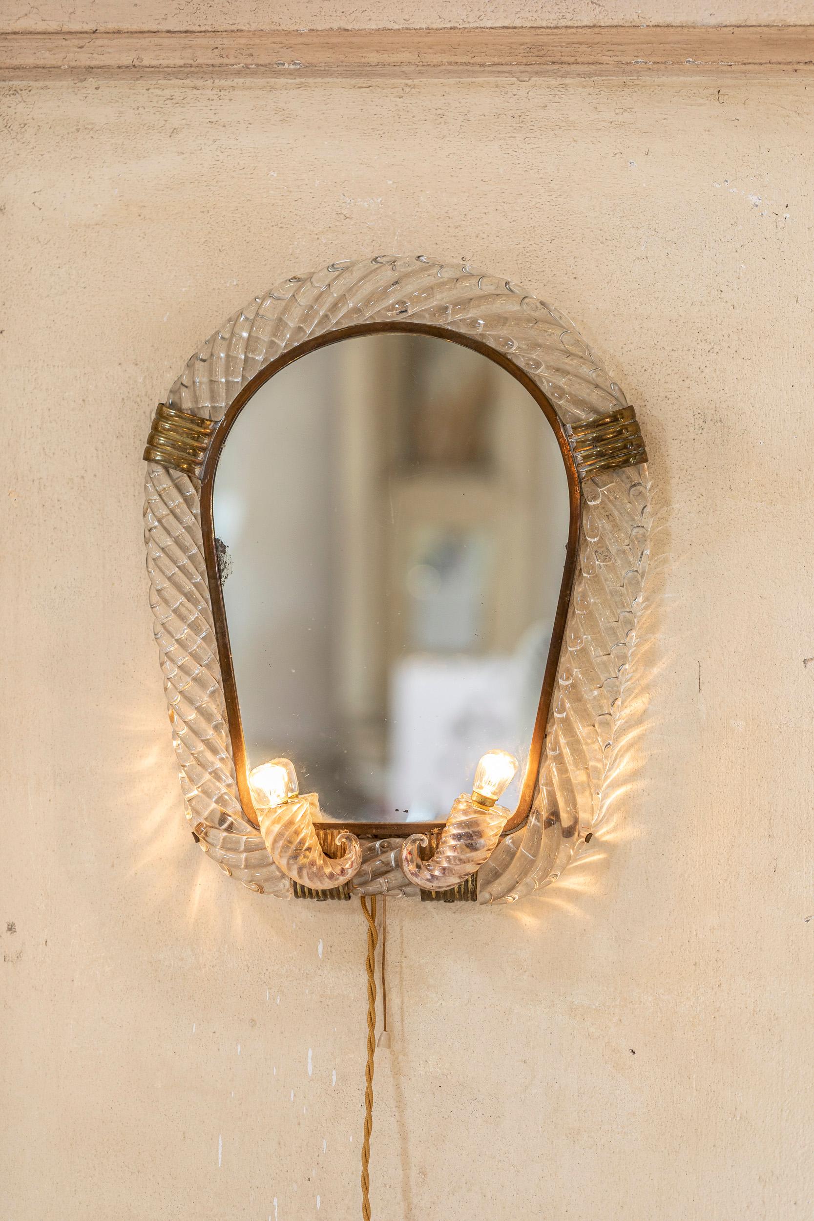 Elegant wall mirror in Murano glass attributed o Gio Ponti for Venini with golden brass details. 
The mirror has two lights in the lower part inserted in two details cornucopia. 
Published on Catalogo Blu Venini.