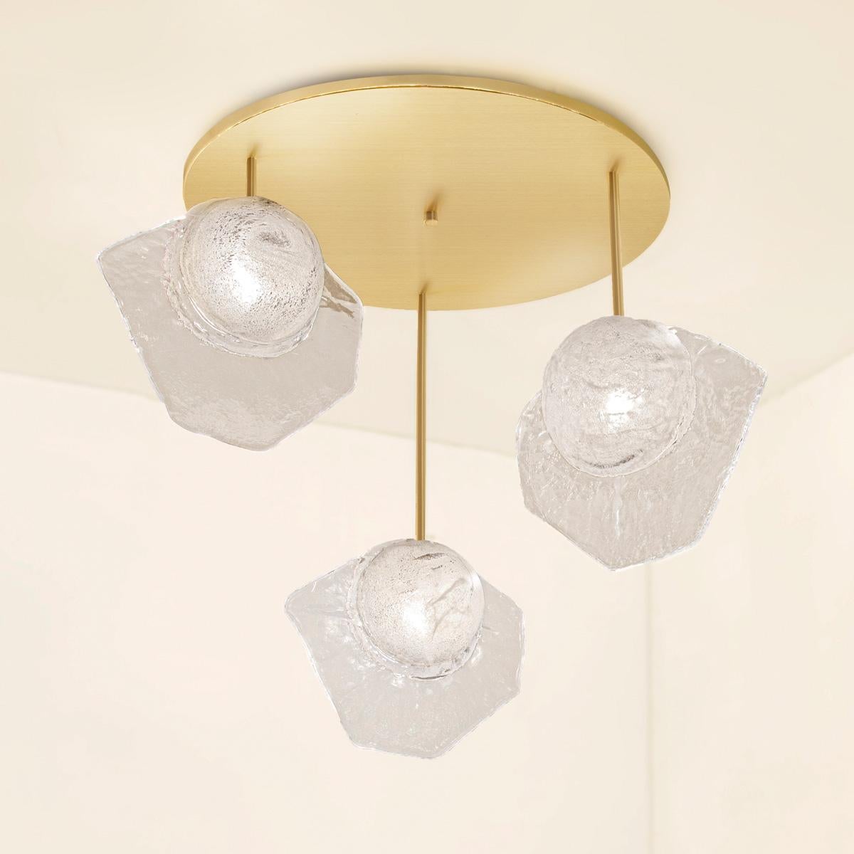 The Vento ceiling light is composed from three or more of our Brezza Murano glass elements hanging from a single canopy. Each hand-blown glass has a bubble infused core and a textured fin. Shown as a composition of three in satin brass. Price listed