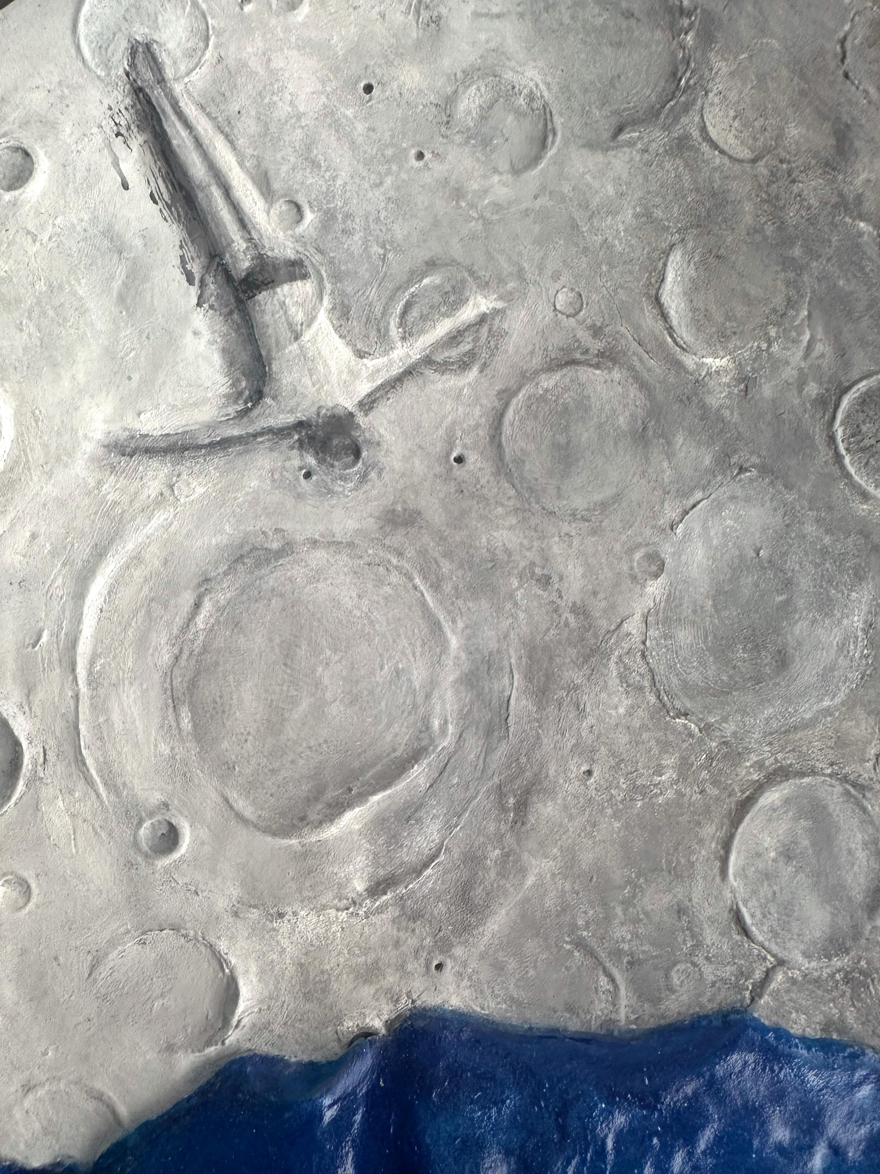 Mondrelief aus Knetmasse mit Acryl auf Holz, das eine kobaltblaue Meereslandschaft darstellt, eine taktile Wandskulptur, die Mondtopografie und Meeresfarben miteinander verbindet. Bei diesem Mondrelief mit gemischten Medien werden Knetmasse und