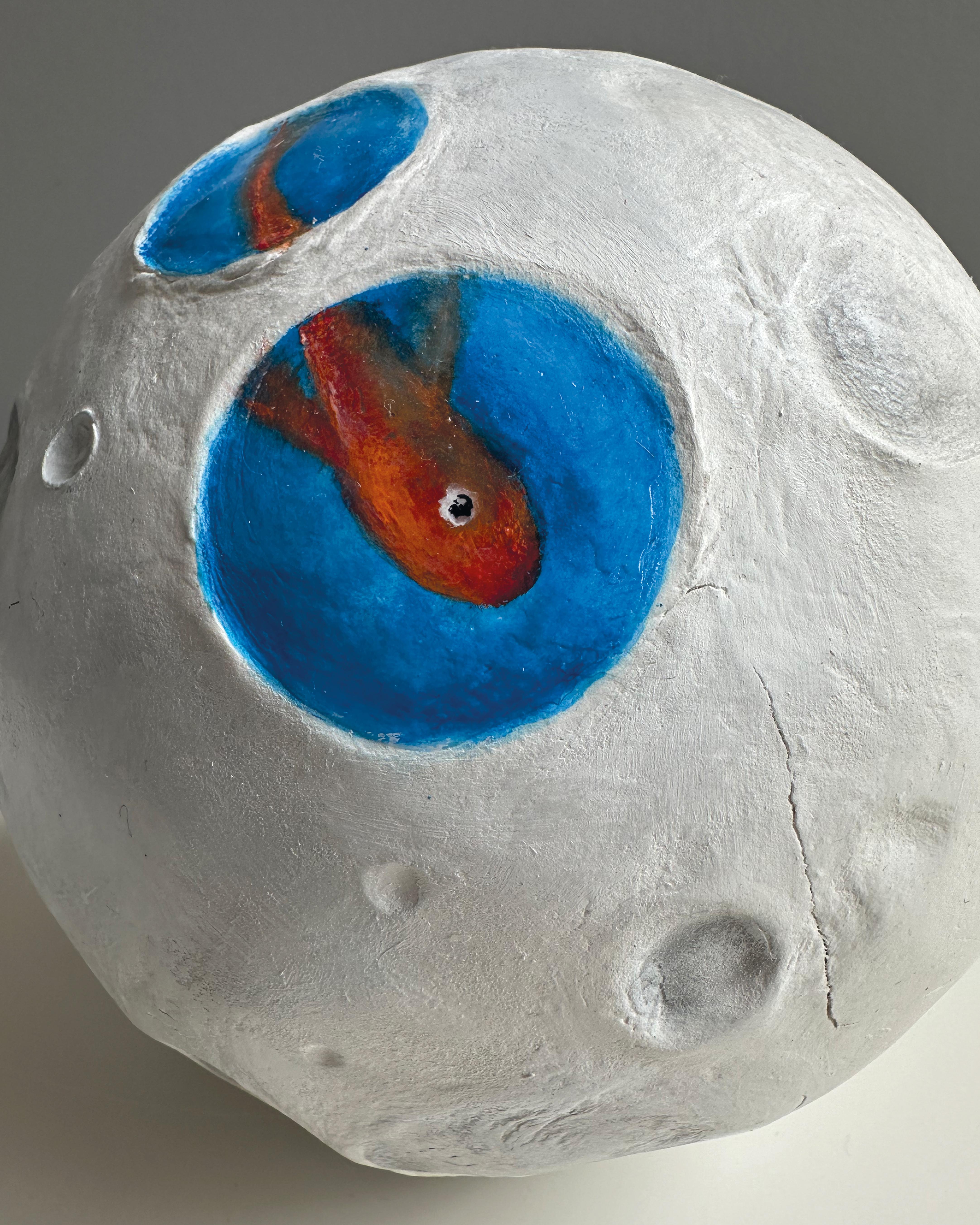 Tutto is a surrealist mixed media sculpture by Vera Vizzi, hand-formed into a lunar sphere with oceanic inlays. Crafted on a 15 cm wood sphere, its cratered white surface evokes the moon, while small round cavities filled with cobalt-blue pigment