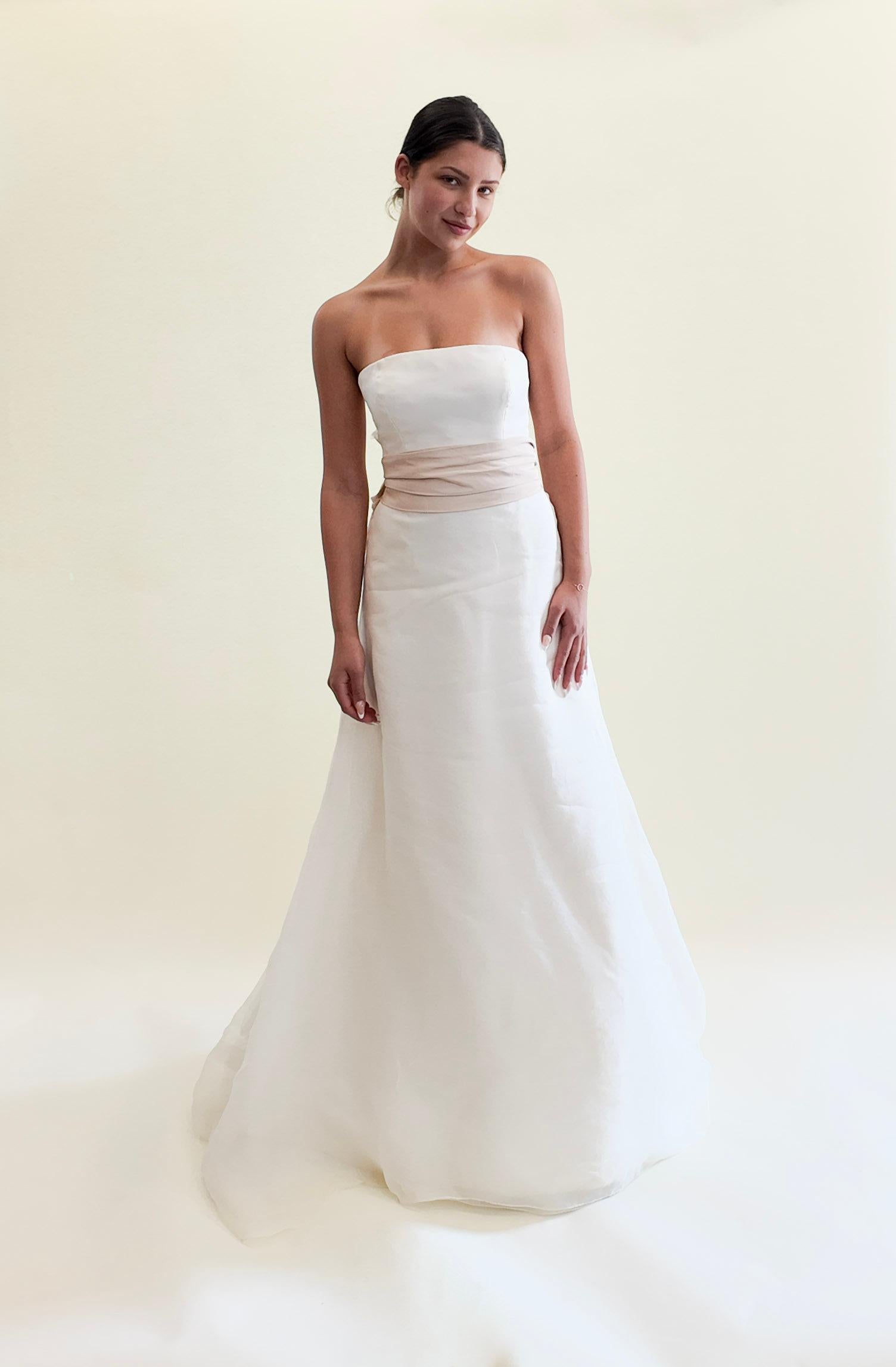 Dieses Vera Wang 2004 trägerlose Seiden-Hochzeitskleid verkörpert eine ätherische Eleganz, die perfekt für die Braut ist, die eine klare, raffinierte Ästhetik sucht. Die zarte Silhouette wird durch eine große, zartrosa Schleife veredelt, die einen