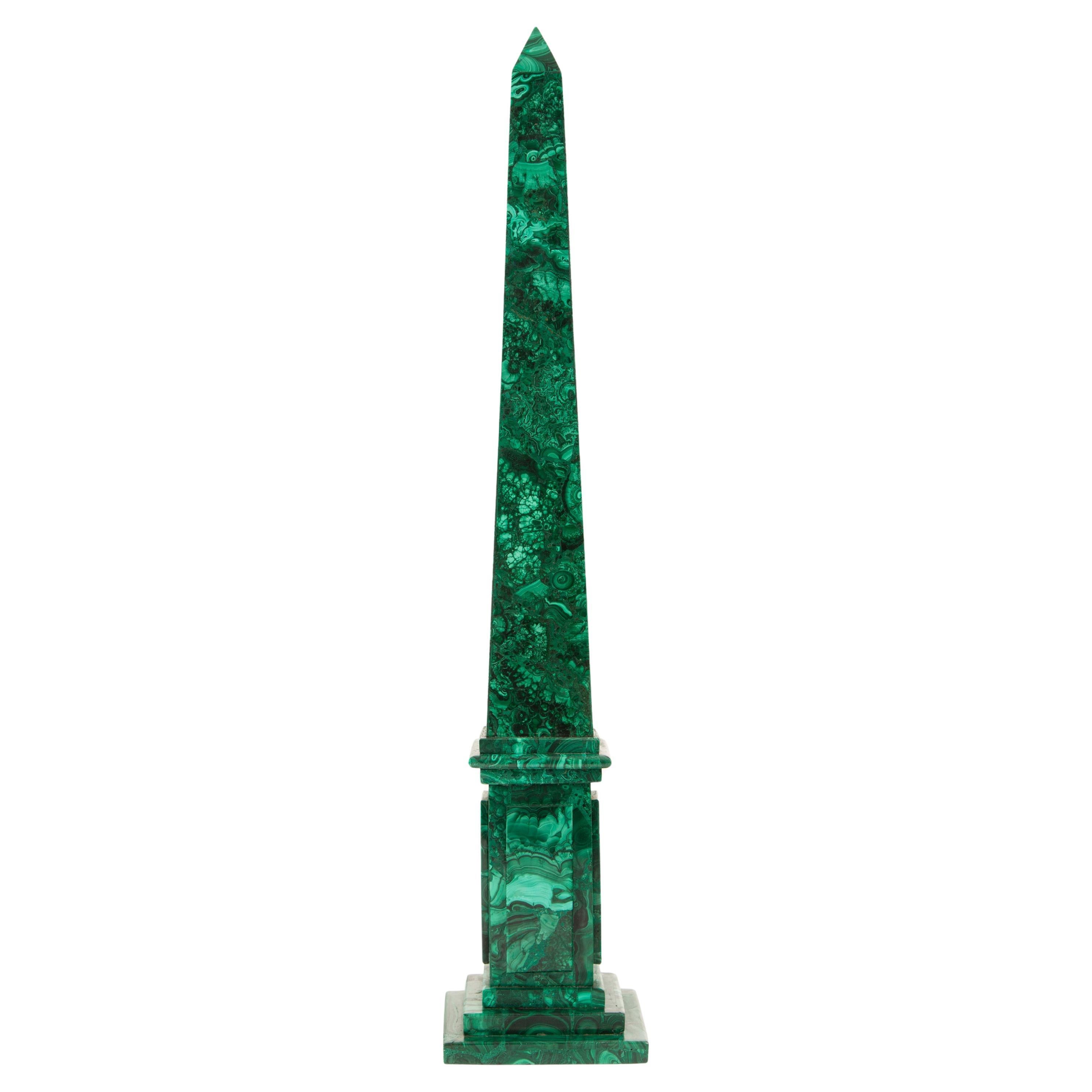 This elegant pair of obelisks is crafted from richly patterned malachite, showcasing the stone's signature swirling bands of deep green and lighter, variegated tones. Standing 19.5 inches tall, each obelisk is constructed in a classic stepped-base