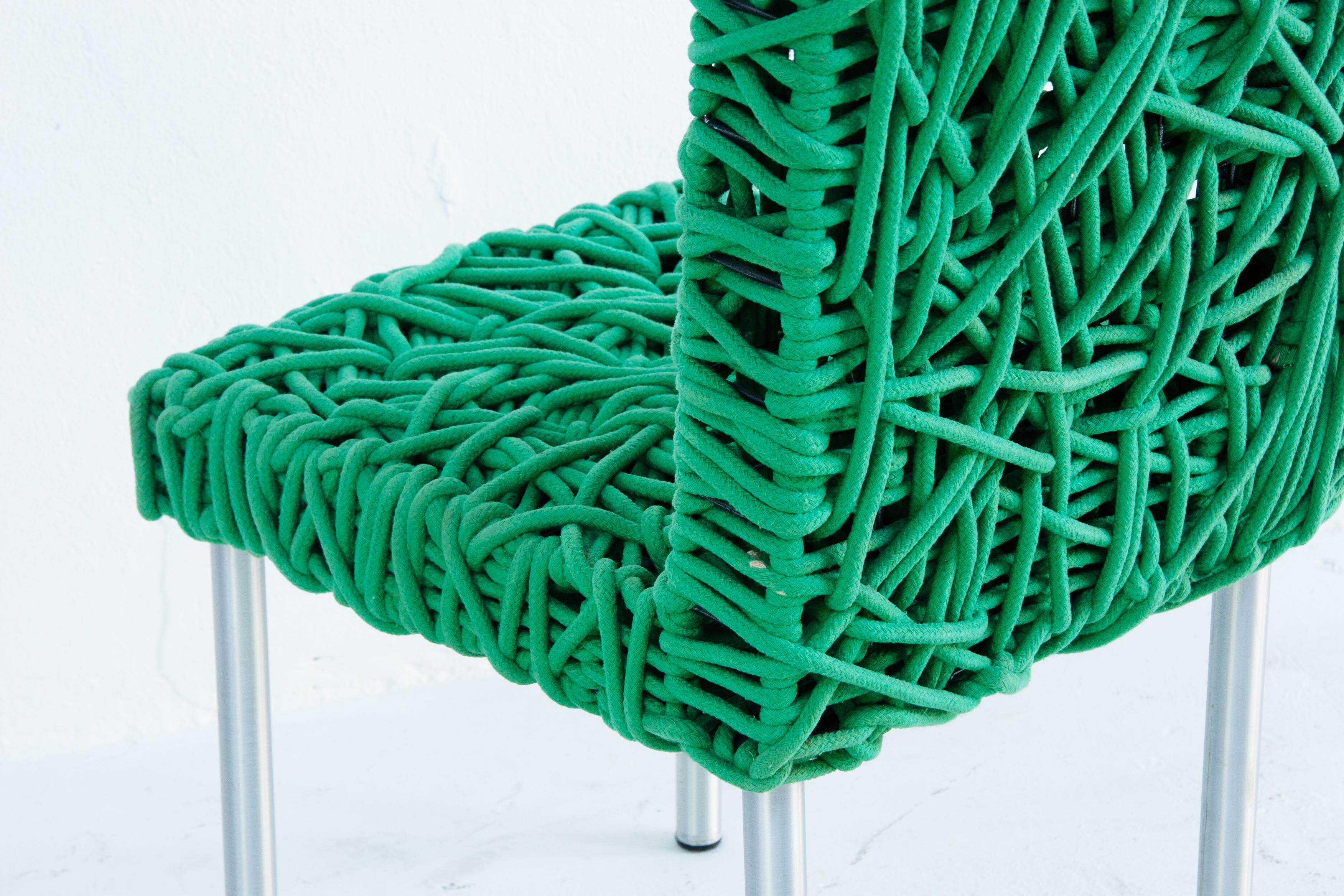 The Verde Side Chair by Campana Brothers for Edra is a unique design piece made with a stainless steel frame and a seat woven from green cotton cords, hand-knotted into a web-like pattern. It creates a playful and whimsical appearance while also