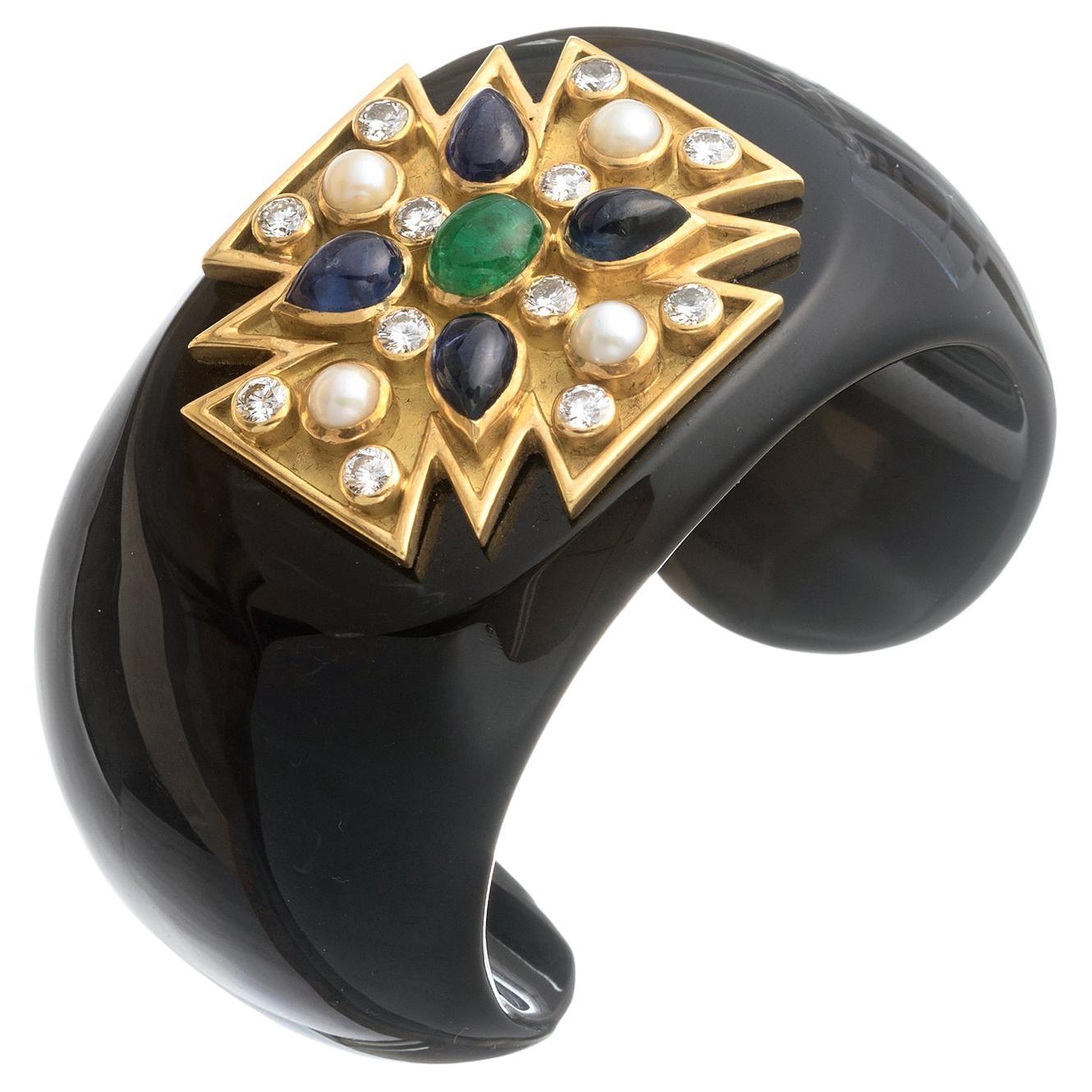 Verdura cuff bracelet, designed as a wide black onyx cuff centering upon an 18k yellow gold Maltese Cross motif set with a larger oval cabochon-cut emerald at center surrounded by four pear cabochon-cut sapphires, as well as twelve round