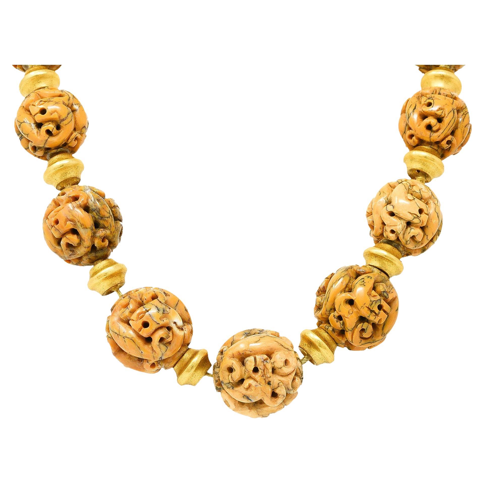 Necklace is comprised of round jasper beads carved to depict animal-like figures and graduating in size from 20.0 to 25.0 mm. Opaque orangey peach in color with white swirling and brownish black veining. Alternating with fluted gold spacer beads -